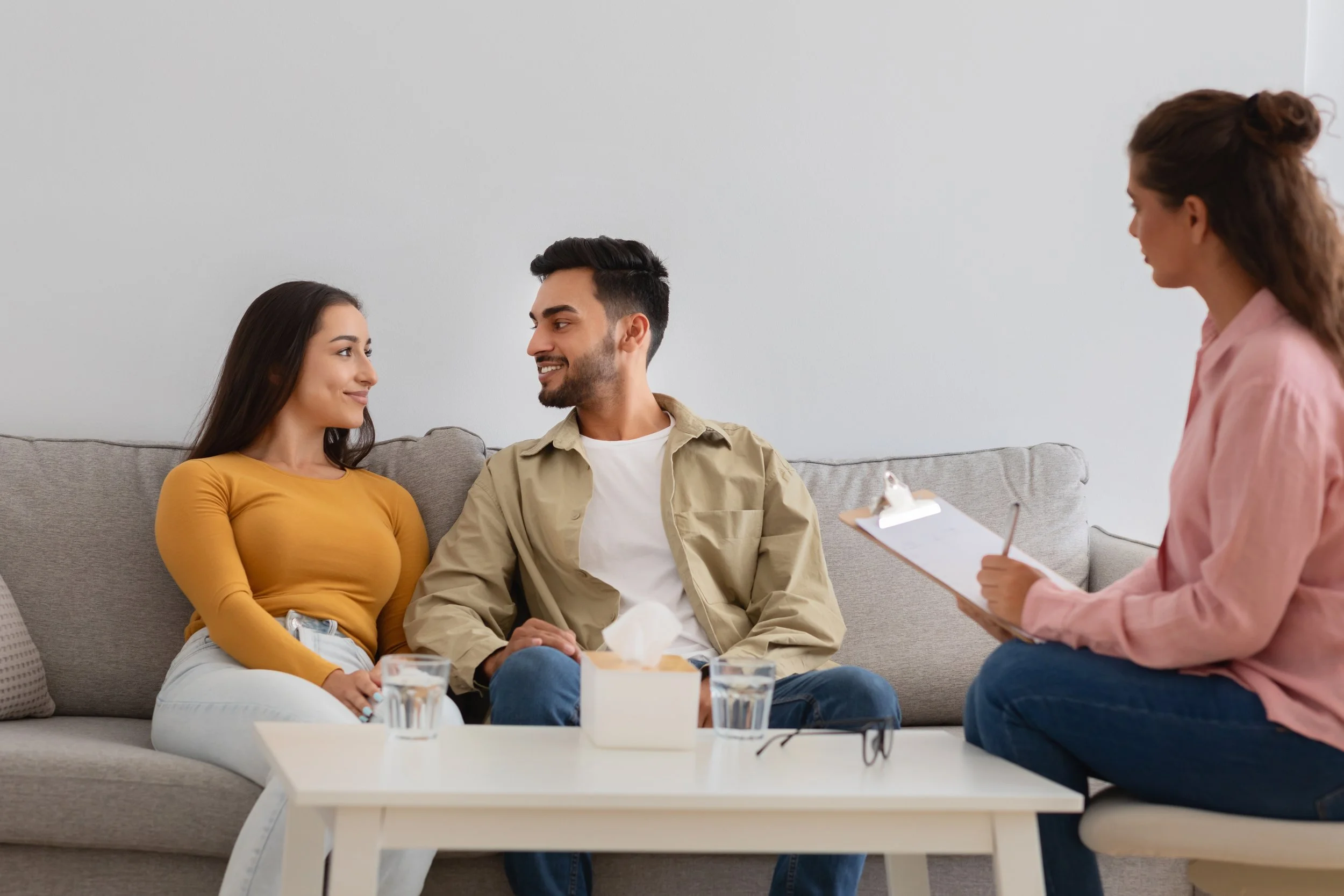 young couple sits on a couch, engaging in a conversation with a therapist