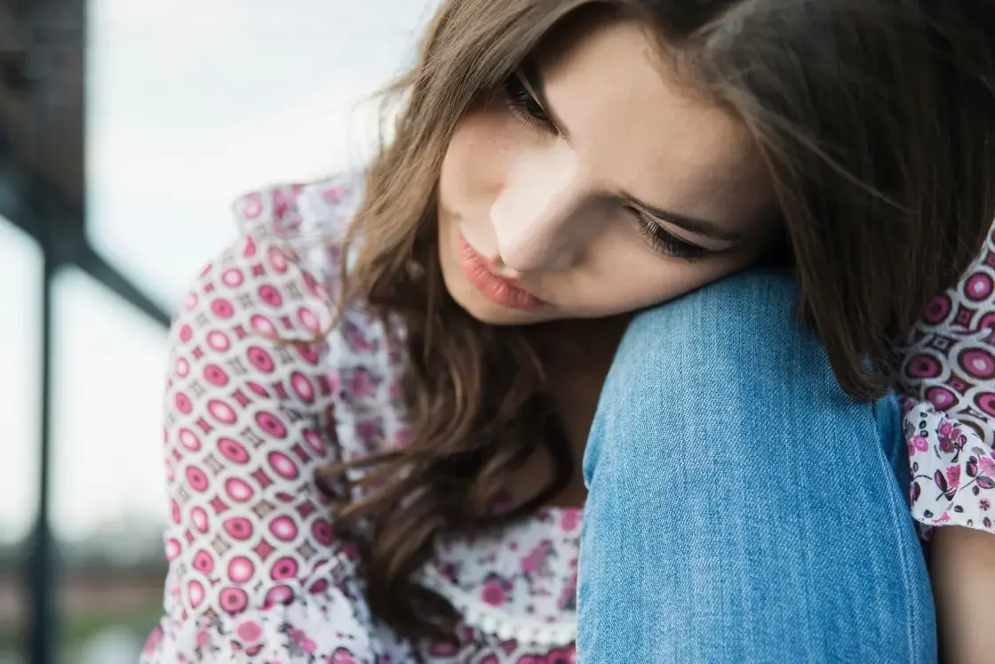 a teenager resting her head on the knees, feeling sad and depressed - a sign for a teenager psychologist help