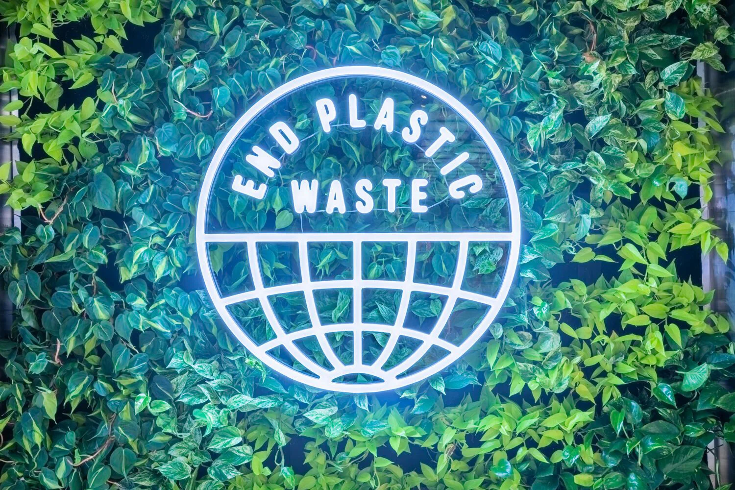 adidas-flagship-store-dubai entrance sustainability messaging, Illuminated end plastic waste signage on a green foliage backdrop