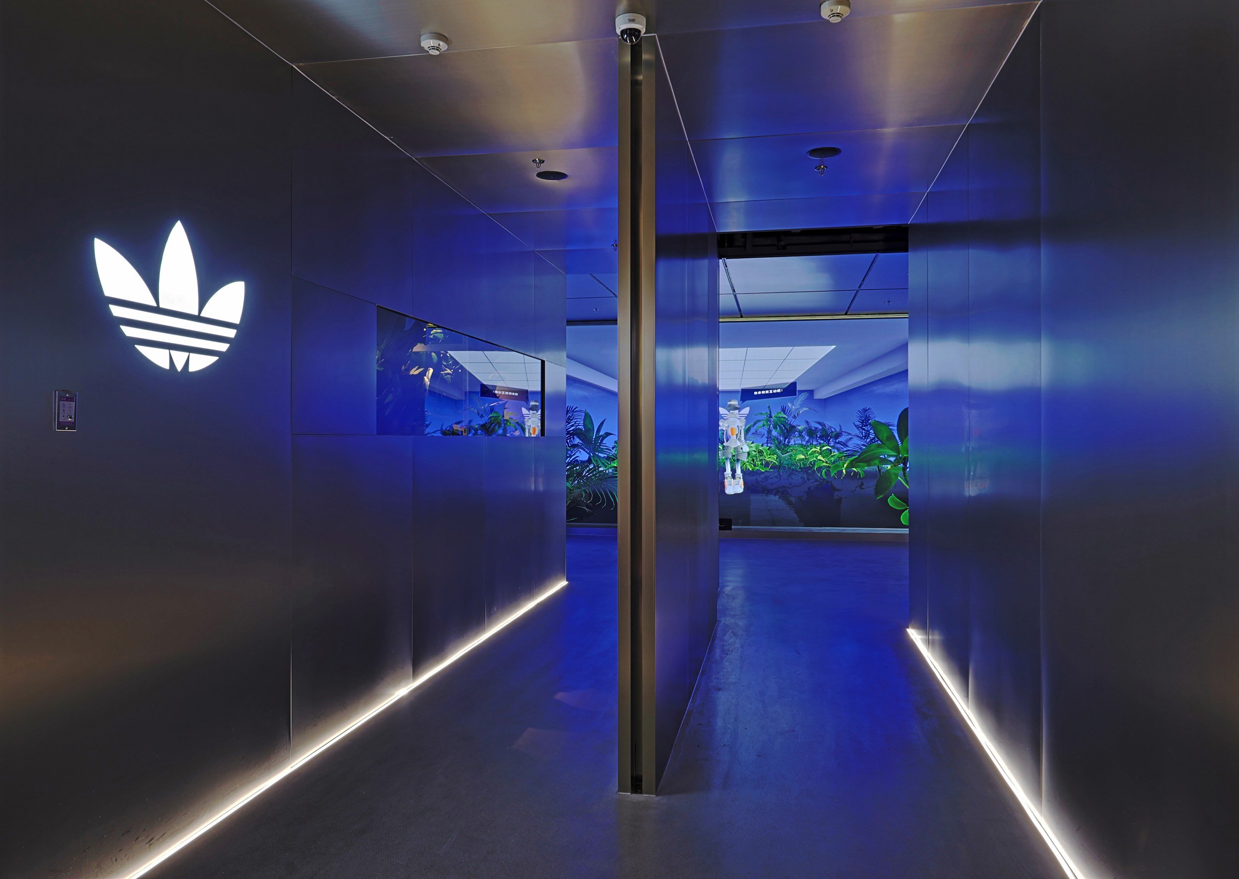 Blue-lit transition corridor inside the Adidas Flagship Sanlitun Beijing with Trefoil branding and immersive lighting.