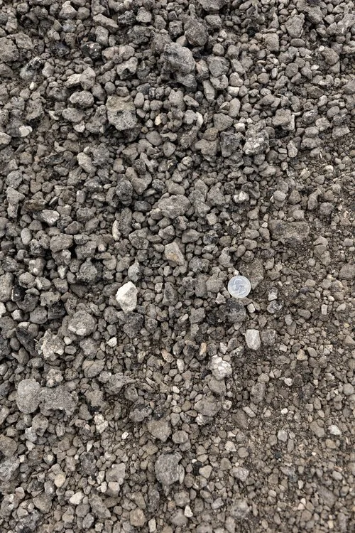 Close-up of dark gray gravel or crushed stone with a coin for scale.