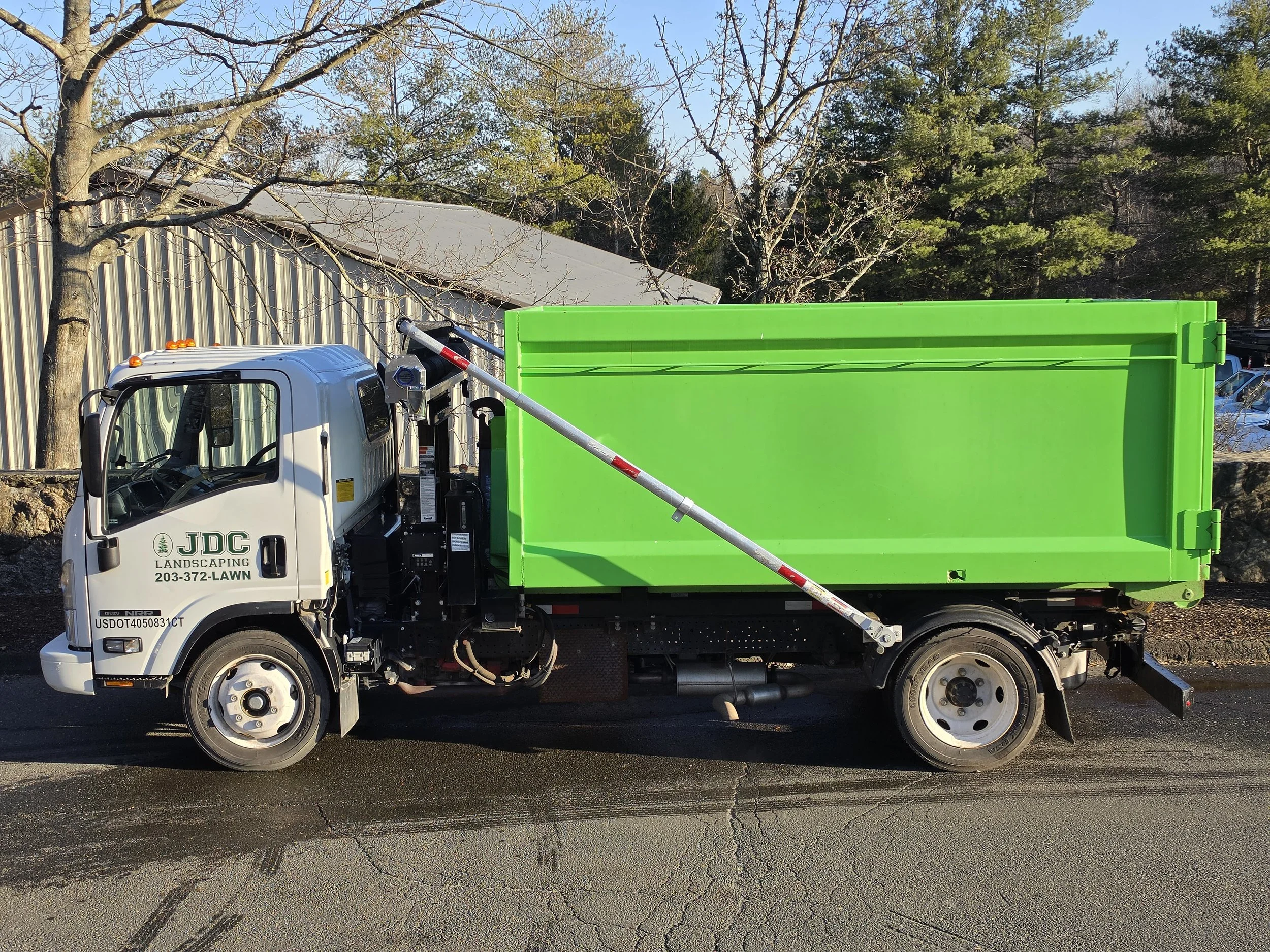 A landscape truck with a white cab and bright green dump bed parked on a street with trees and buildings in the background.