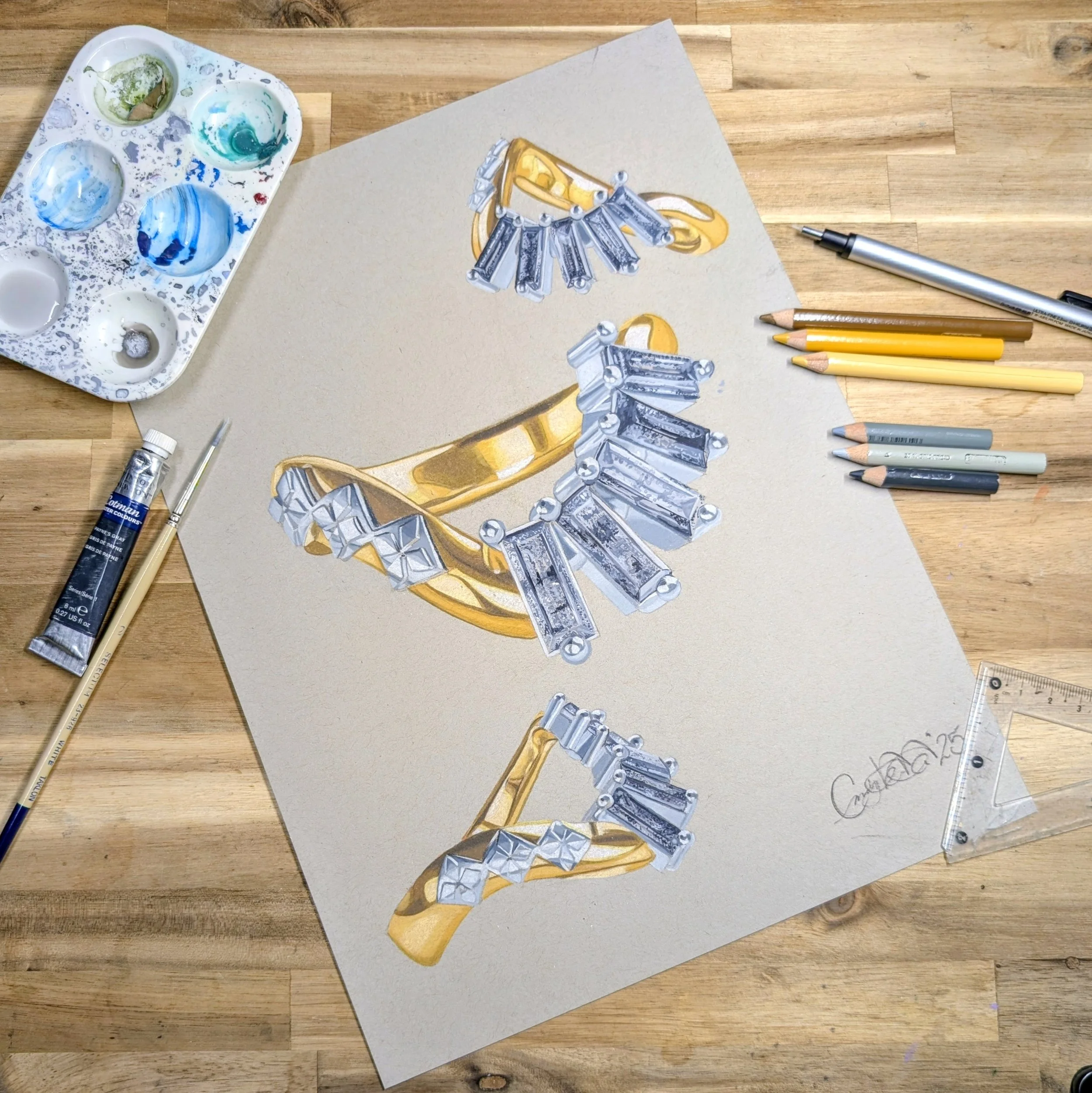 A detailed drawing of gold and diamond jewelry signed by the artist, surrounded by colored pencils, a paint palette with mixed colors, a ruler, and pens, on a wooden surface.