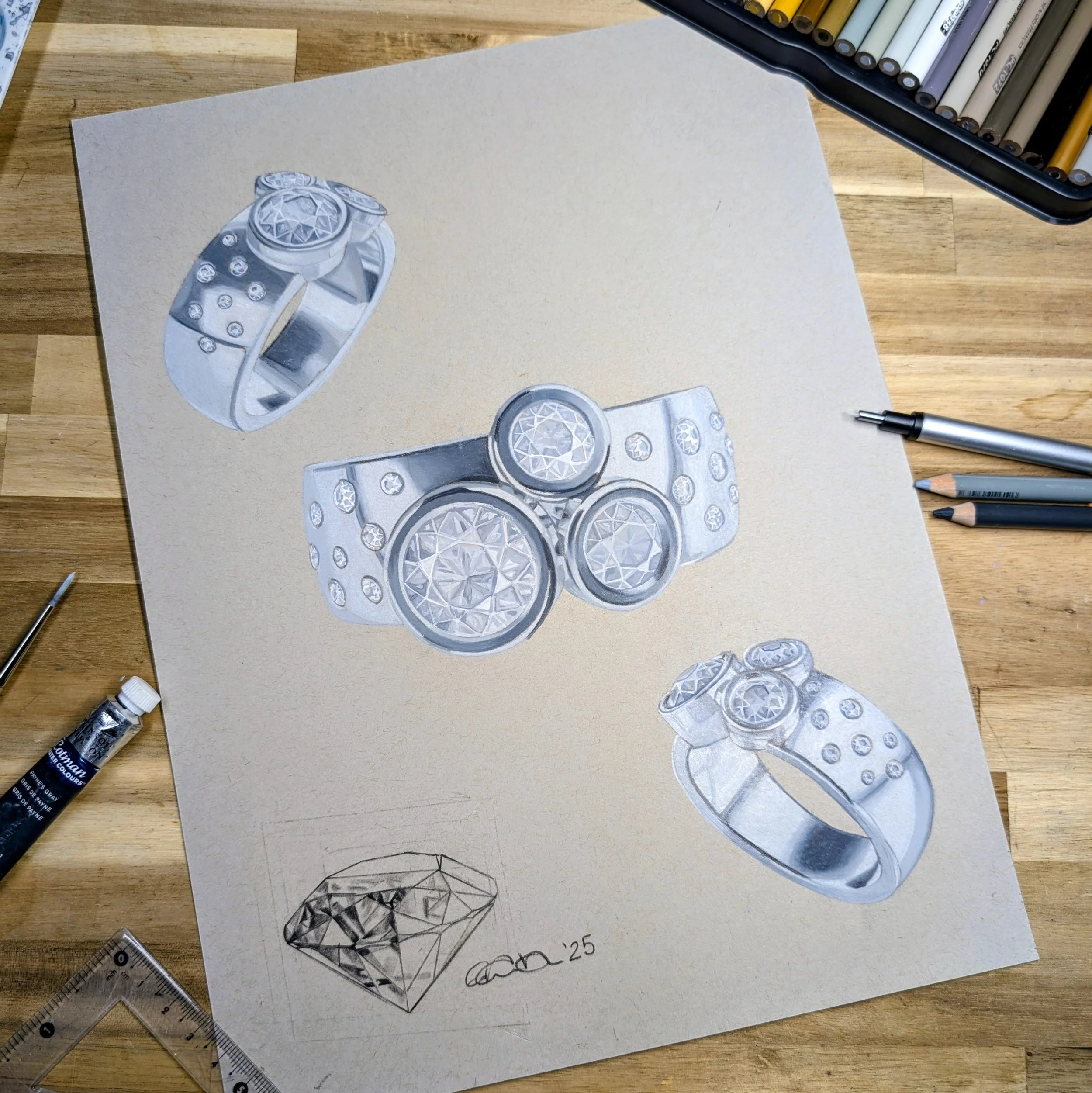 A detailed drawing of three rings with diamond-like decoration, and a sketch of a diamond on paper, on a wooden table with drawing tools and colored pencils around.