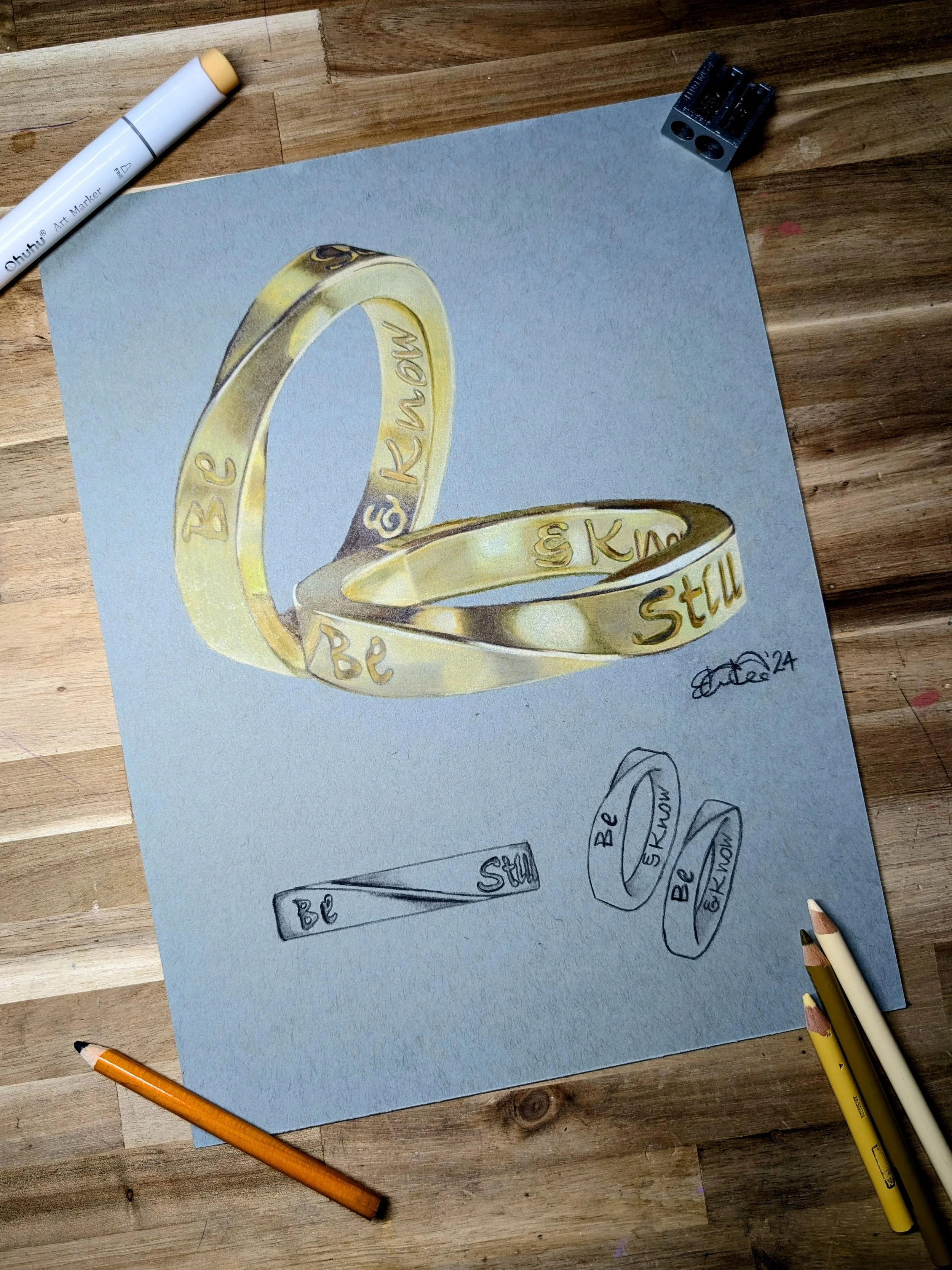 Hand-drawn illustration featuring a ring with engraved words, along with sketches and notes about the design process, on a blue sheet of paper on a wooden surface.
