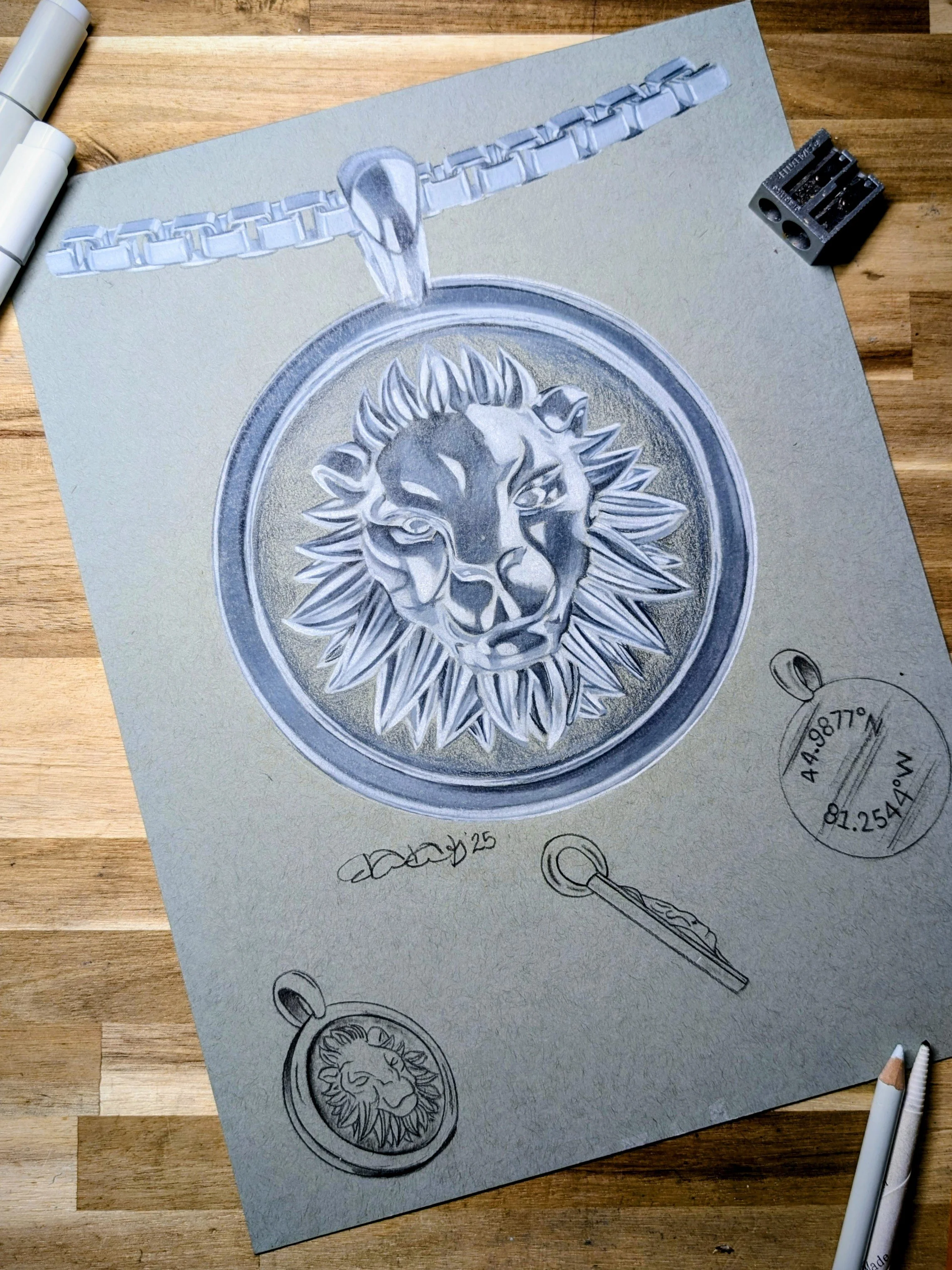 A detailed sketch of a lion's head in a circular pendant, with a chain at the top, alongside sketches of a key and a round tag with GPS coordinates.