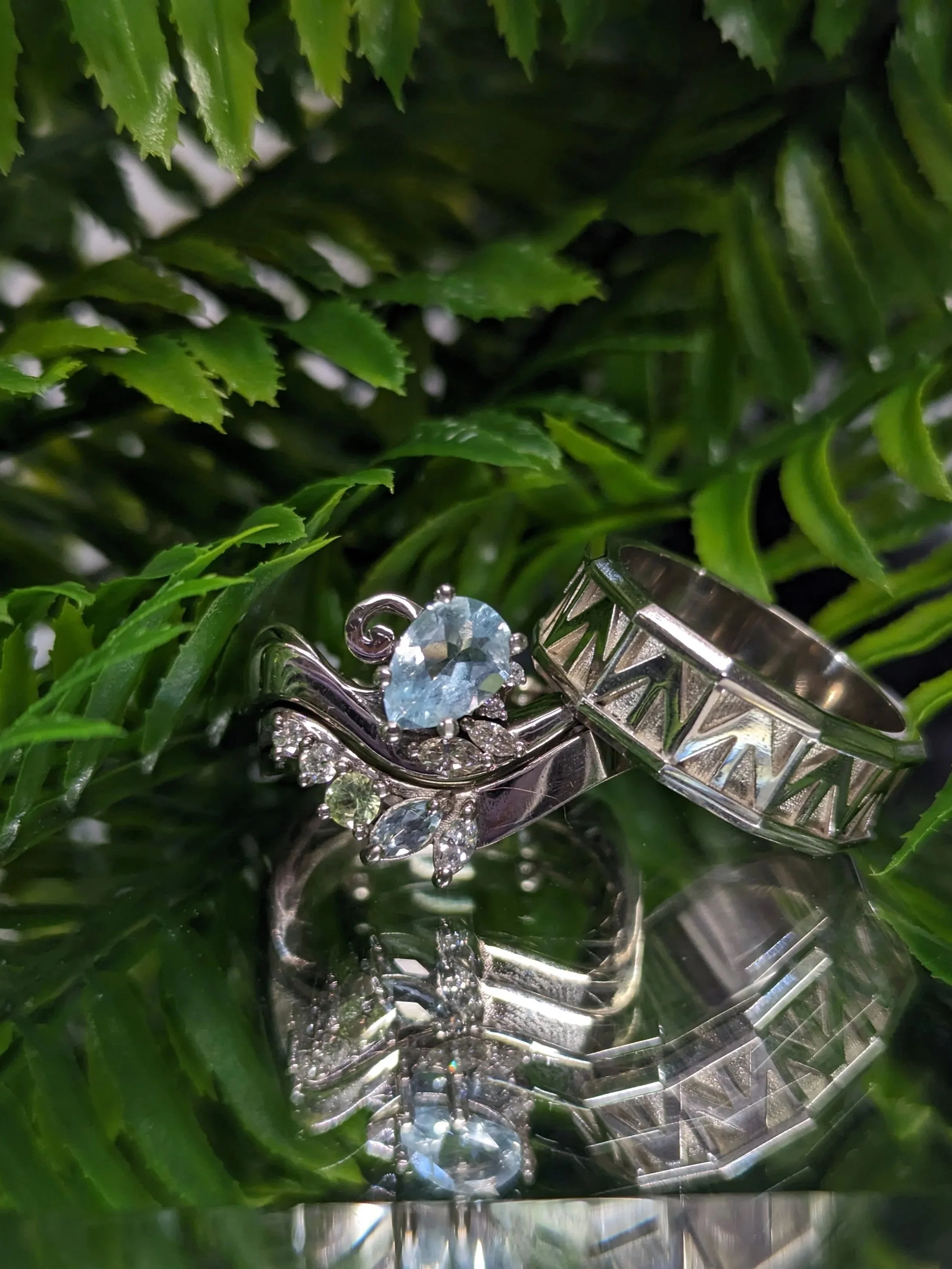 white gold wedding band  set featuring the engagement ring with a pear shaped aquamarine, with accent marquise cut and round diamonds. The ladies wedding band features a curved design with a mixture of diamonds, peridot, and aquamarine.