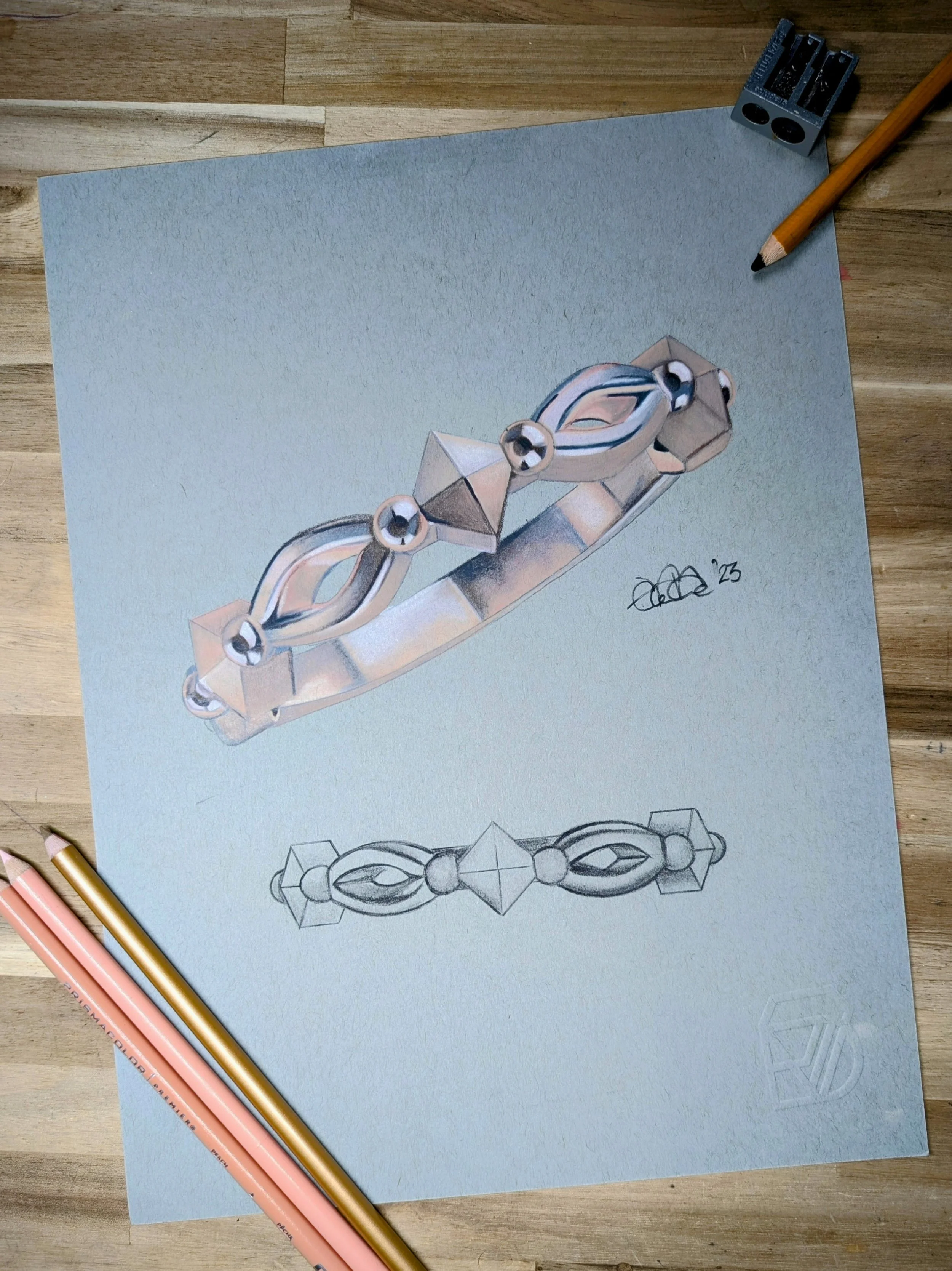 A detailed drawing of a rose gold ring  with geometric and oval-shaped elements, shown both as a colored illustration and as a pencil sketch, on a desk with pencils and a sharpener.