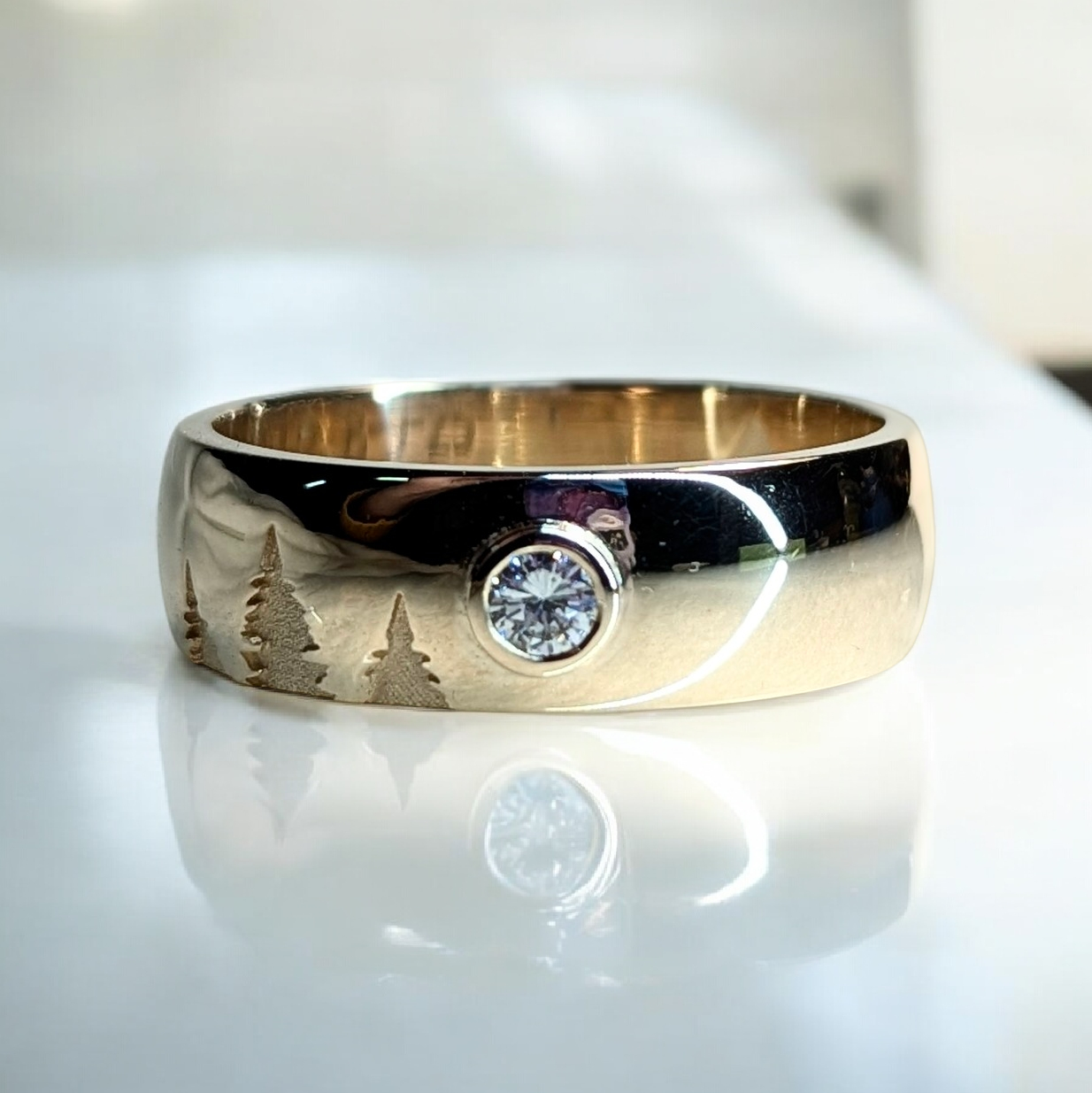 Yellow gold mens wedding band featuring three pine tree cut out details and a bezel set round brilliant diamond in the center