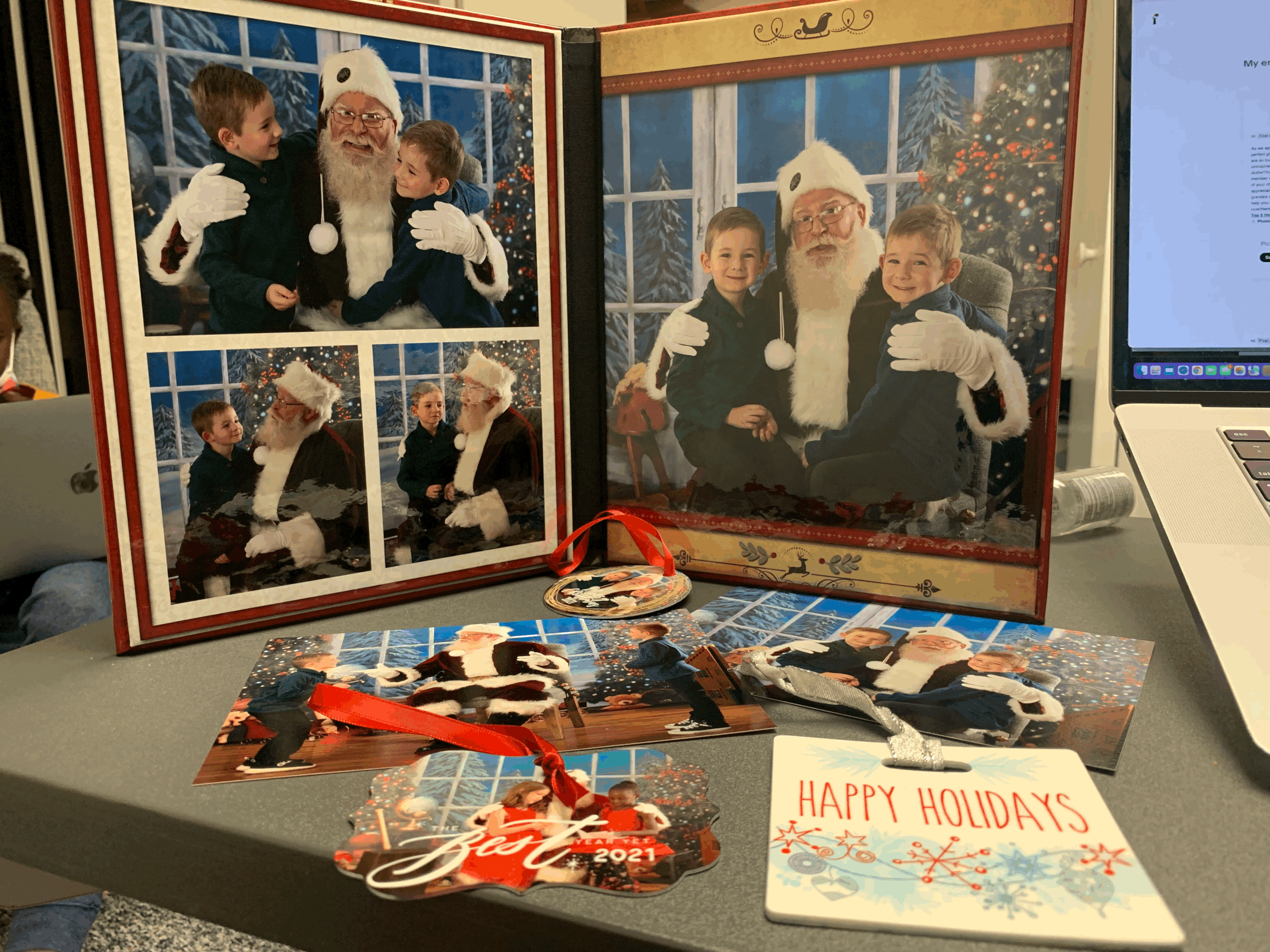 Collage of holiday photos featuring two children with Santa Claus, accompanied by festive ornaments and a "Happy Holidays" card on a gray table.