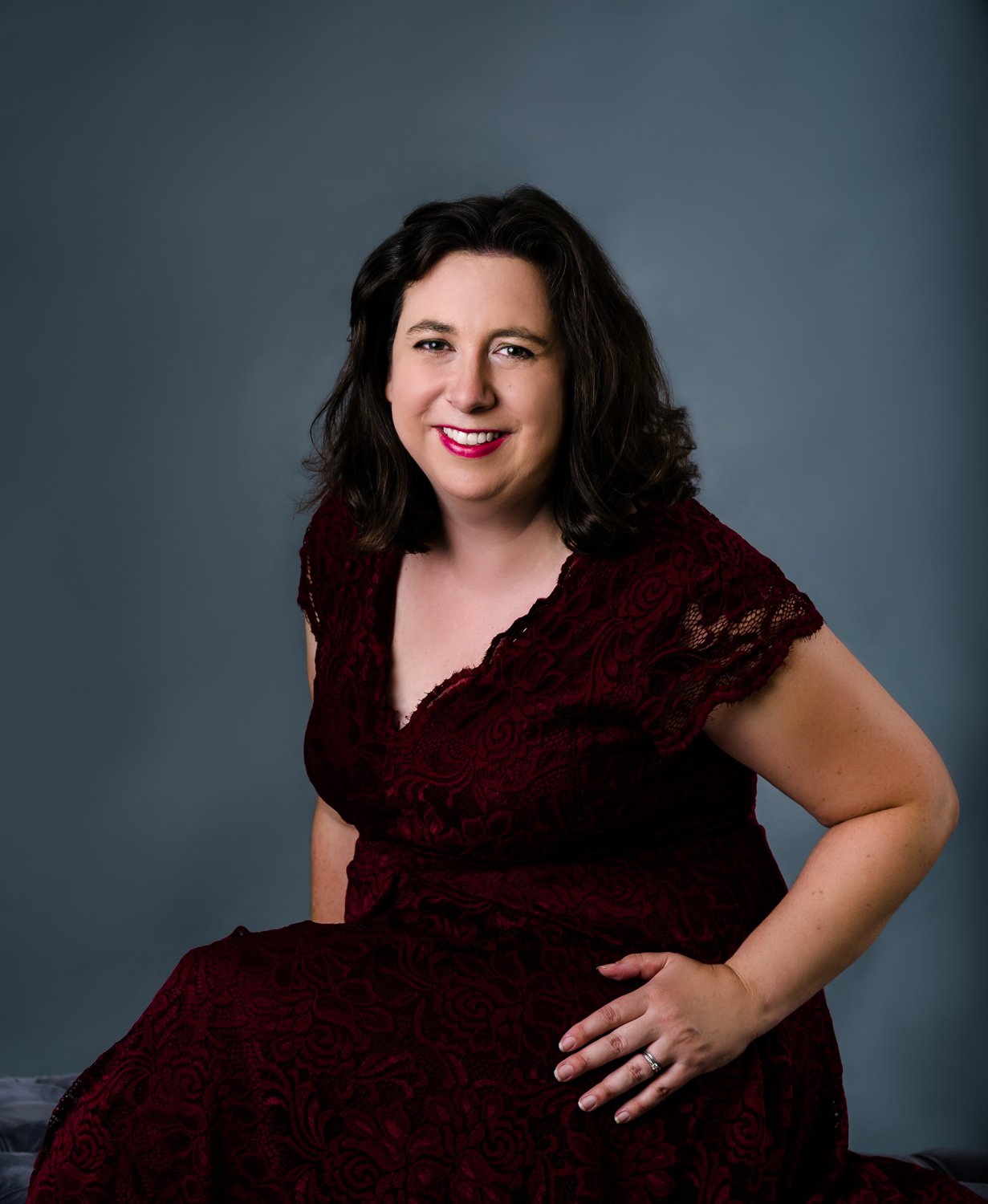 Smiling woman in a red lace dress with a dark background.