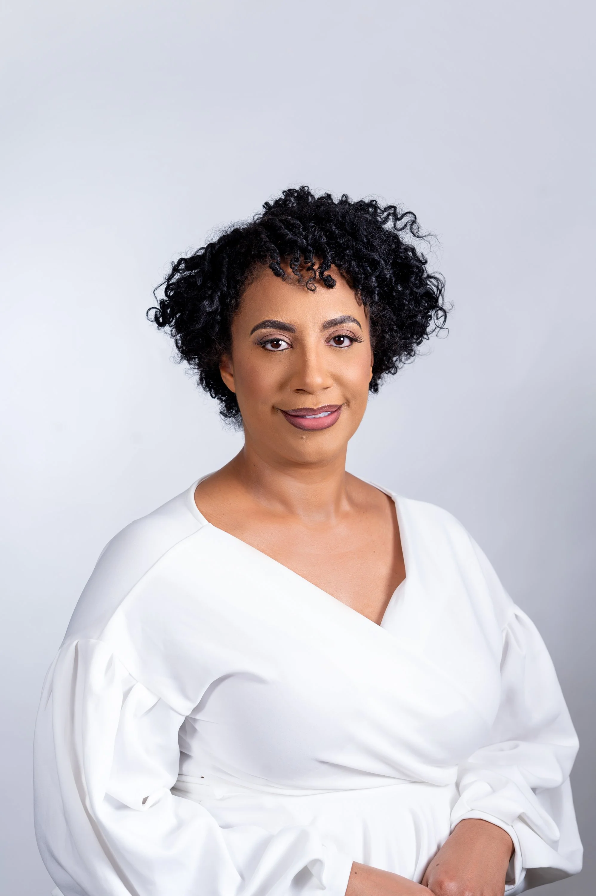 Woman with curly hair in white top against neutral background