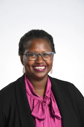 Person wearing glasses, black blazer, and magenta blouse with a bow.
