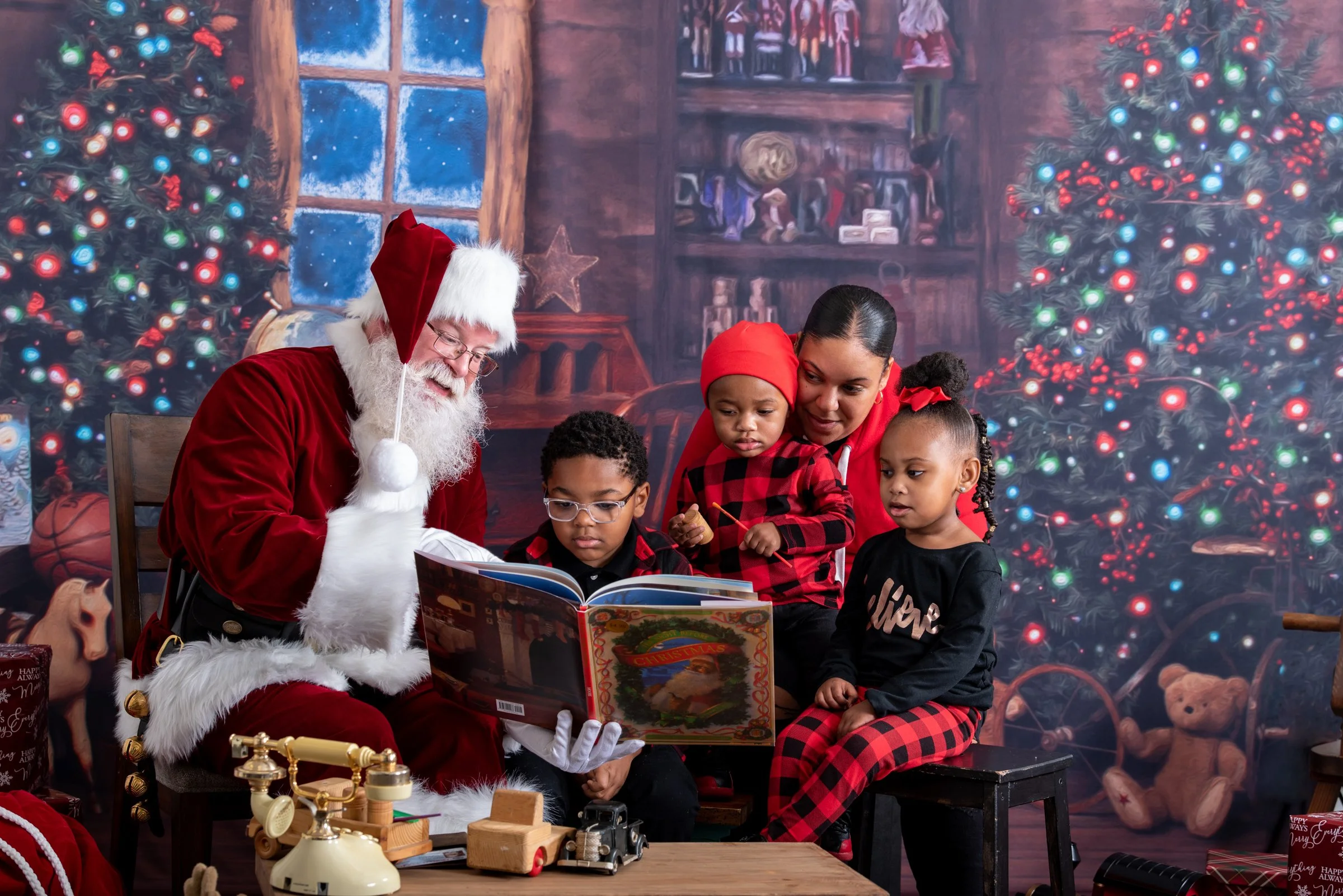 Santa Claus reading a book to three children and an adult in a festive room with a decorated Christmas tree, toys, and gifts.