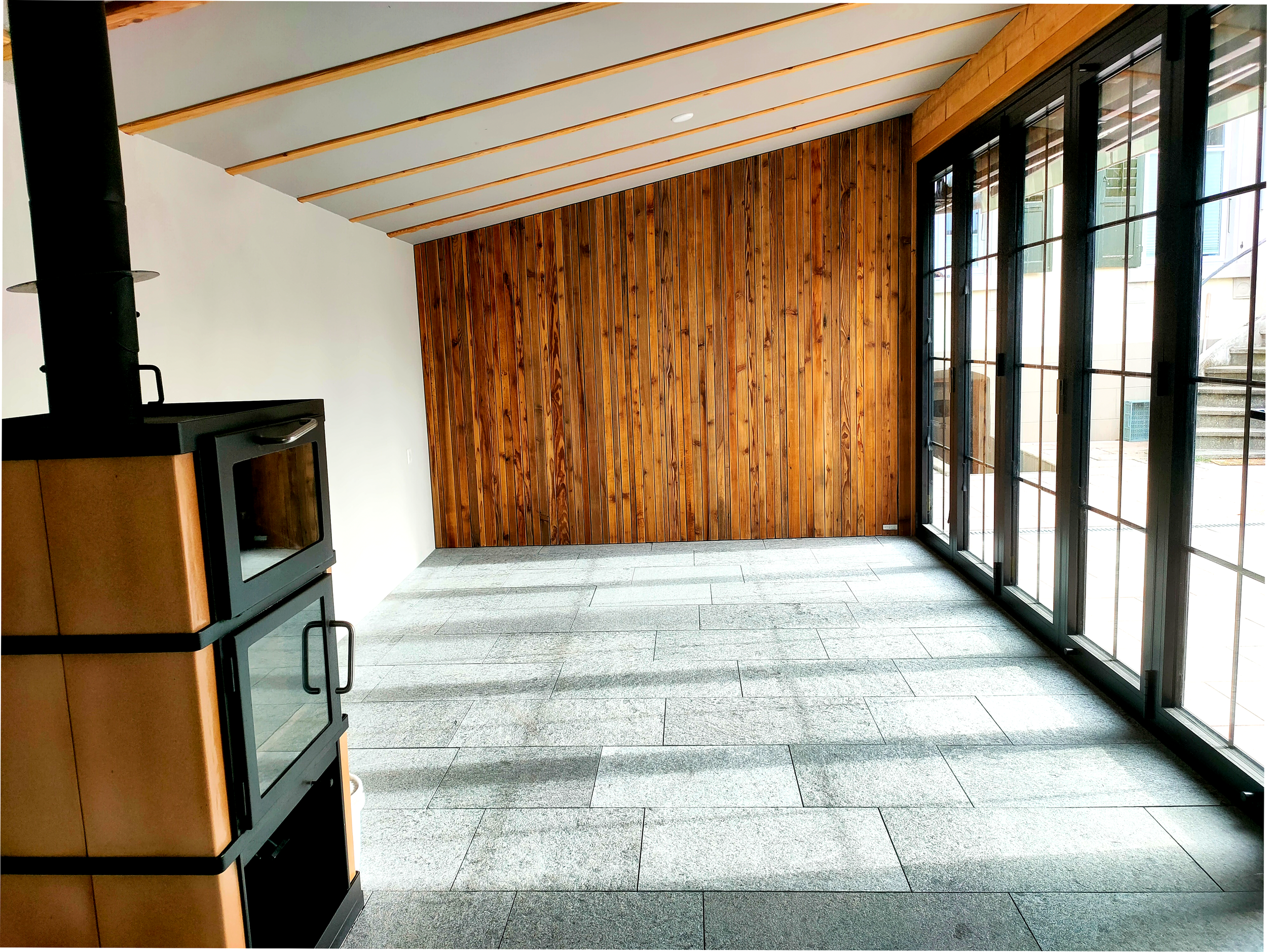 Lichtdurchflutender Wintergarten mit Faltschiebewand, Kamin, Natursteinbelag aus dem Onsernonental und Altholzverkleidung, Thun und Umgebung