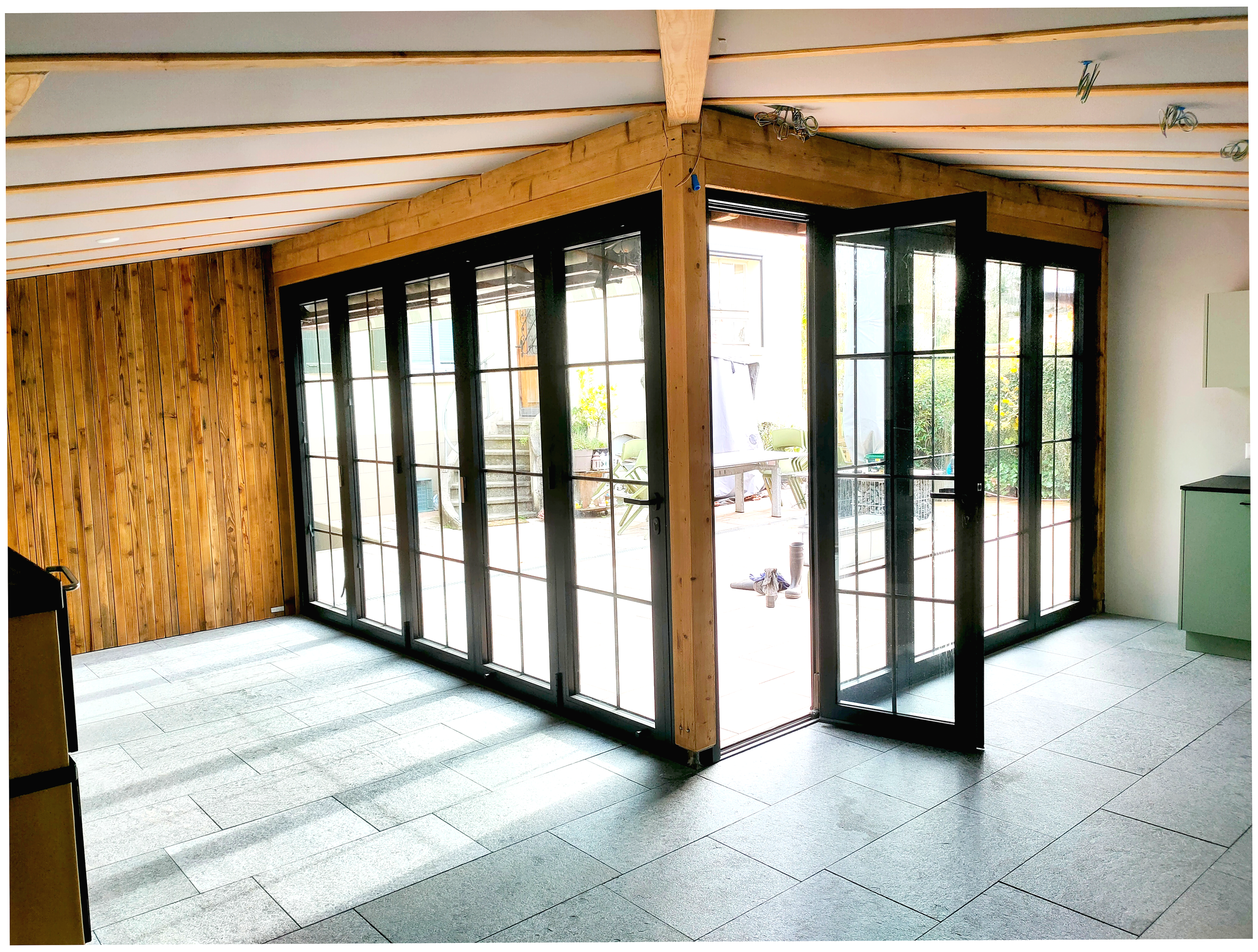 Fensterfront,Faltschiebewand, Wintergarten in schwarzer Ausführung, Deckenbalken gebürstet,Natursteinboden aus der Schweiz, Thun