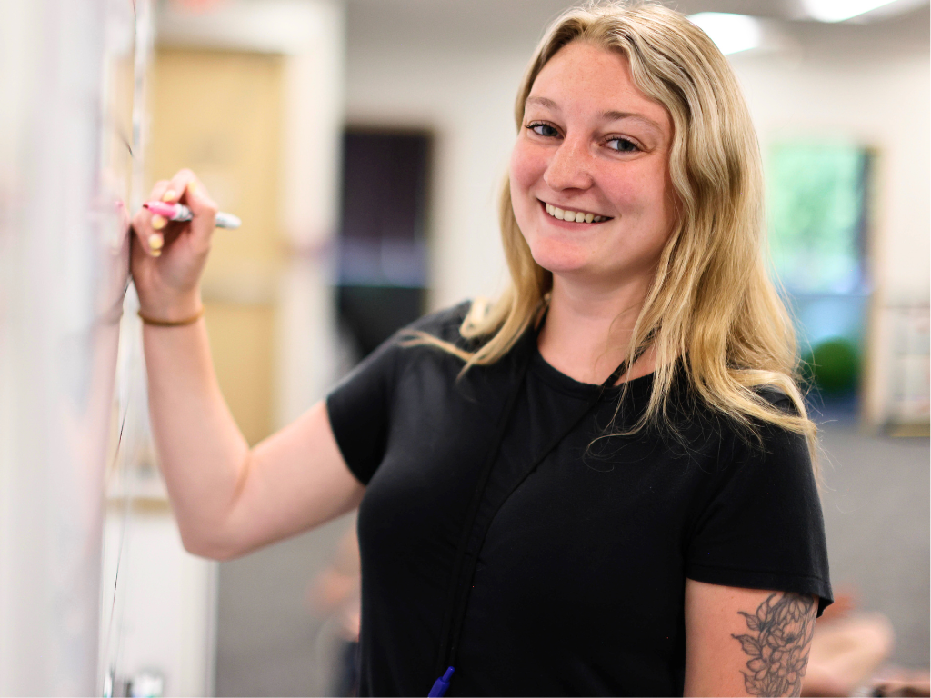 Crossroads Continuum staff member leading a classroom activity, writing on a whiteboard in a supportive, inclusive learning environment.