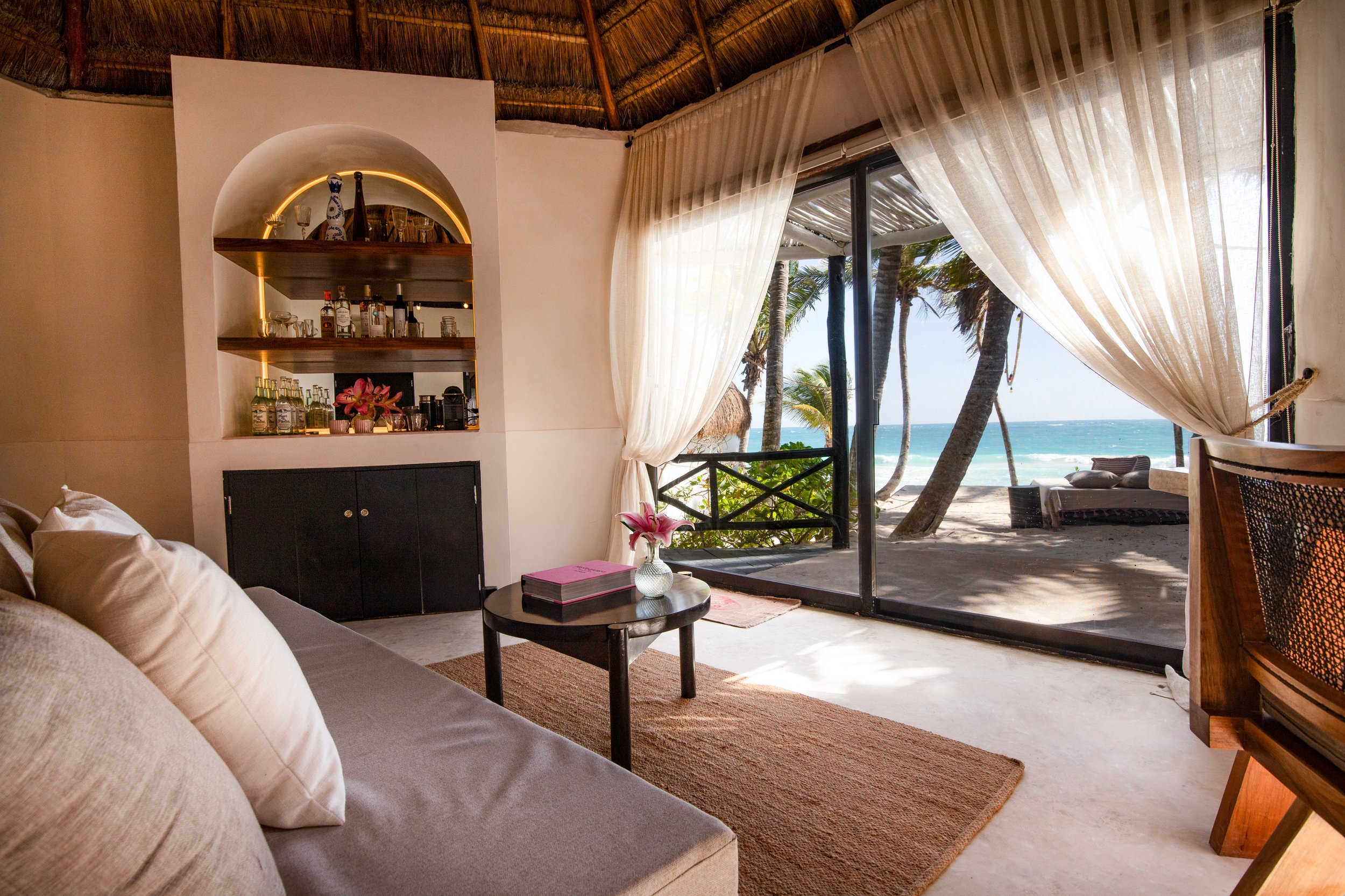 Interior of beachfront suite with bar, sofa, and ocean view through sliding glass doors at Casa Gitano Tulum