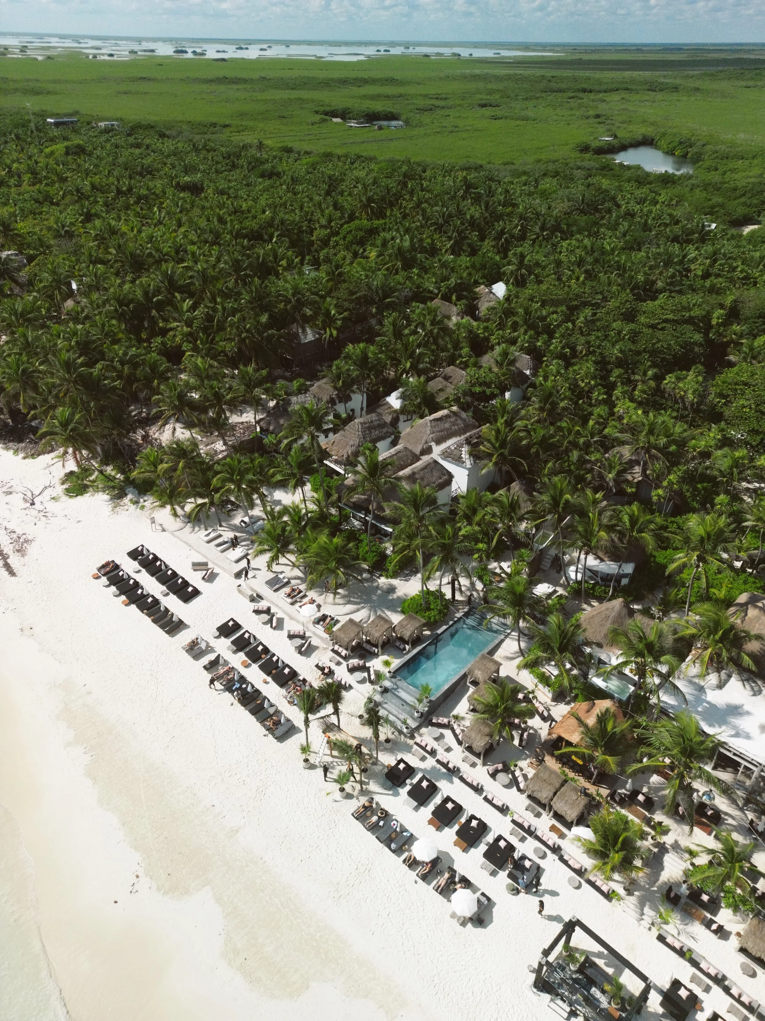 Beachfront view of CASA GITANO in Tulum, with pristine white sand, swaying palm trees, and chic private villas steps from the turquoise sea.