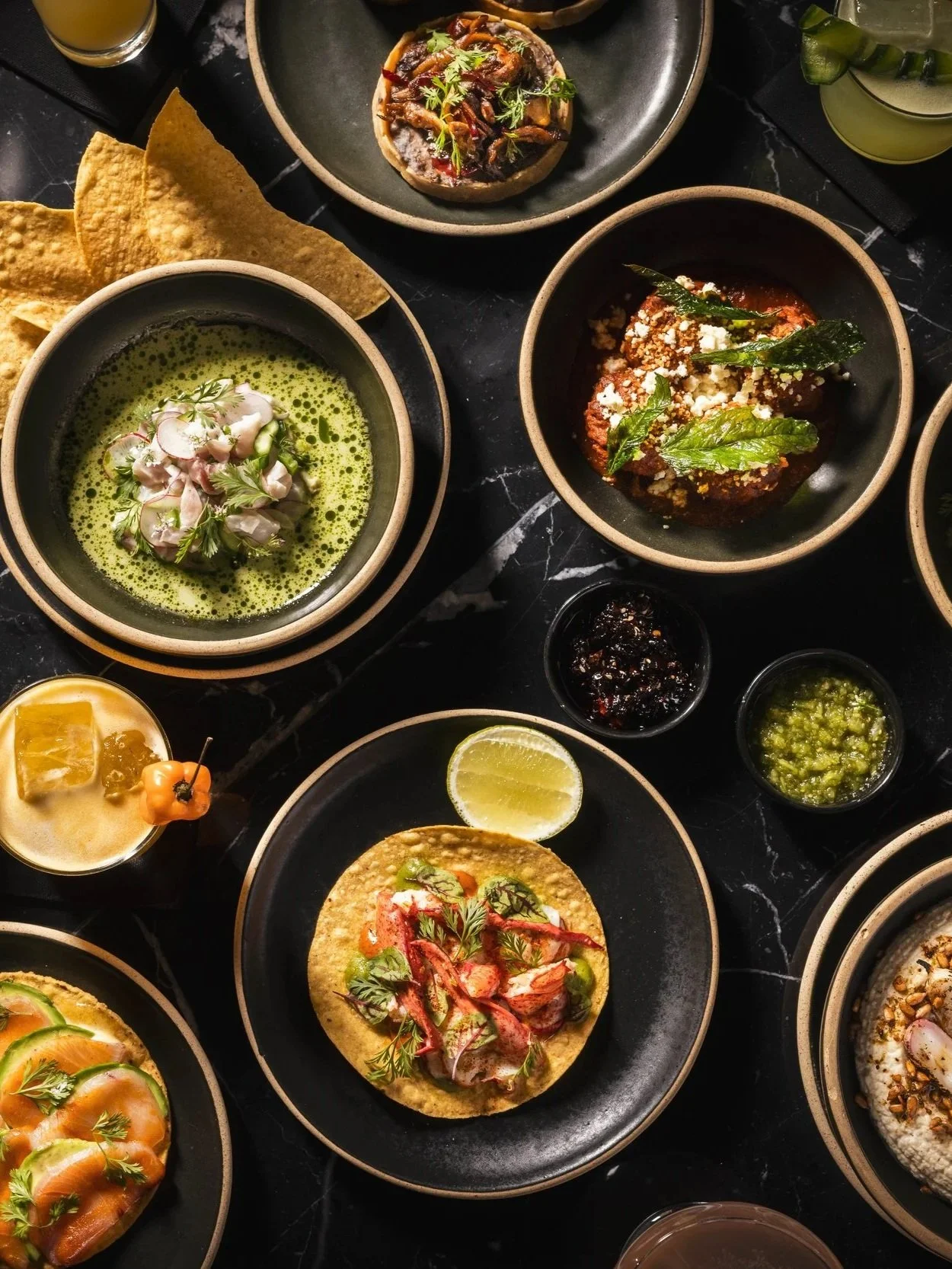 Daylight fills the dining room at GITANO NYC, where lush tropical plants, bohemian décor, and sweeping views of the Brooklyn Bridge create an elegant waterfront oasis.