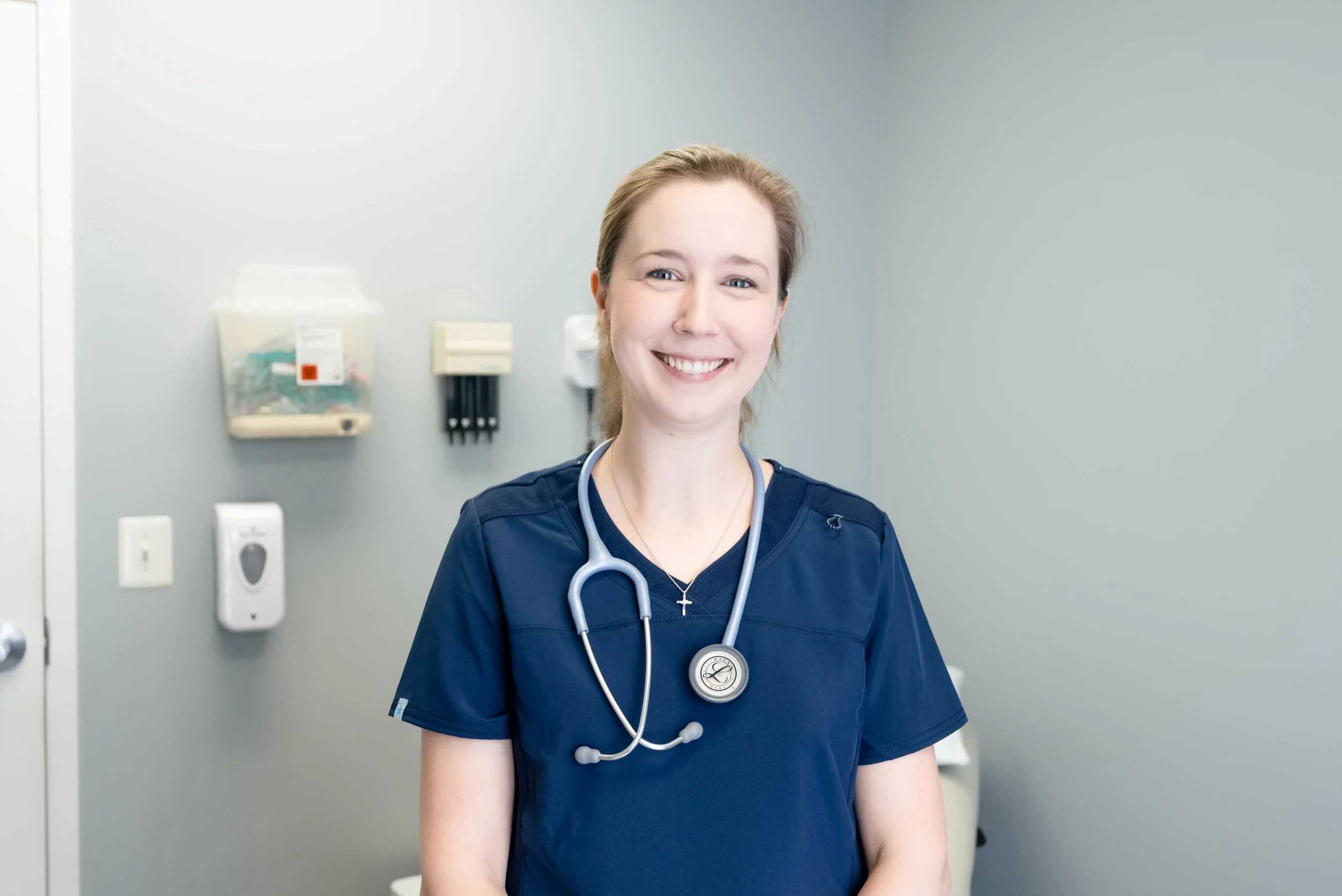Smiling nurse or healthcare professional with stethoscope in clinic room.