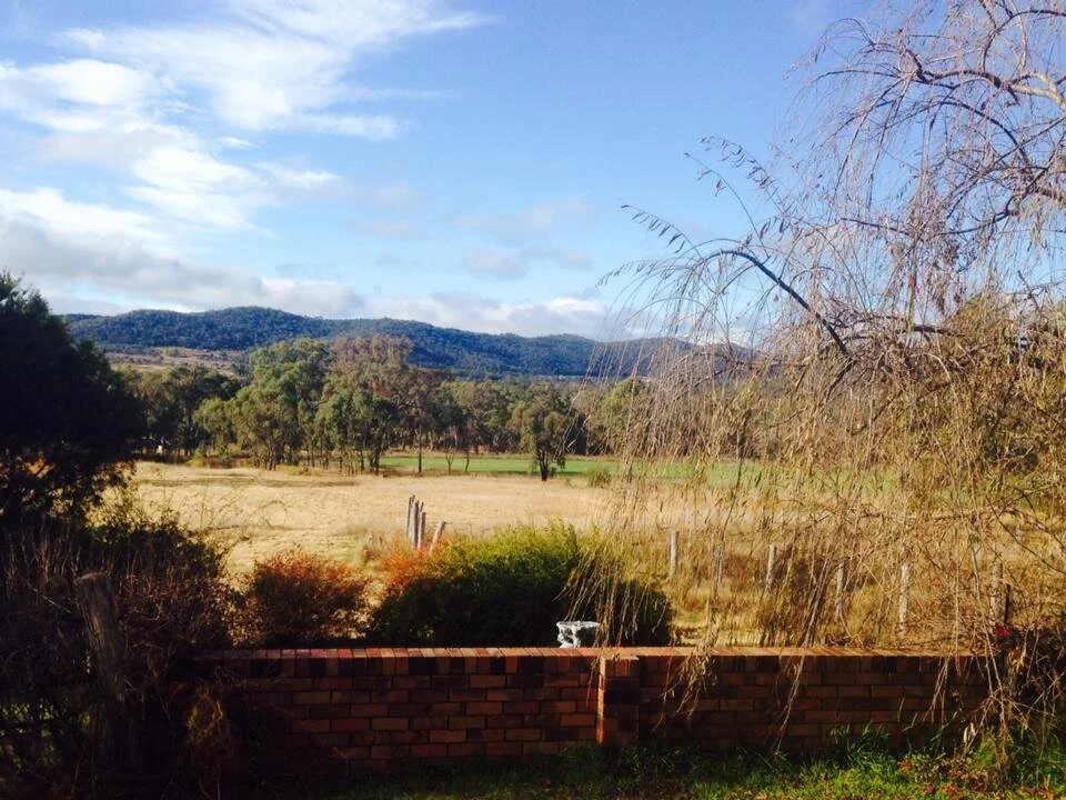 View of a rural landscape with grassy fields, trees, distant hills, a brick wall in the foreground, and a partly cloudy sky.