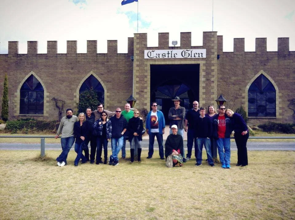 Group of people standing in front of Castle Glen building with a sign above the entrance, castle-like brick structure, arched windows, and flags on top.