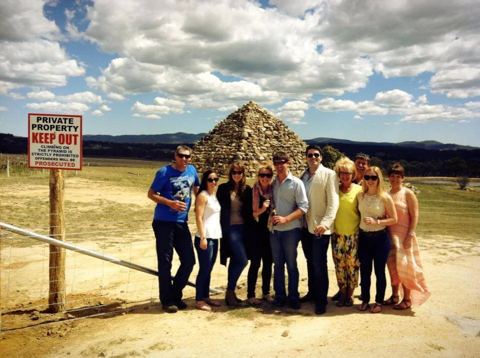 Group of nine people standing outdoors in front of a stone pyramid with a cloudy sky background, next to a red and white private property sign.