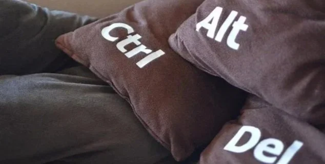 Two brown pillows with white labels reading 'Ctrl', 'Alt', and 'Del' on a dark-colored surface.