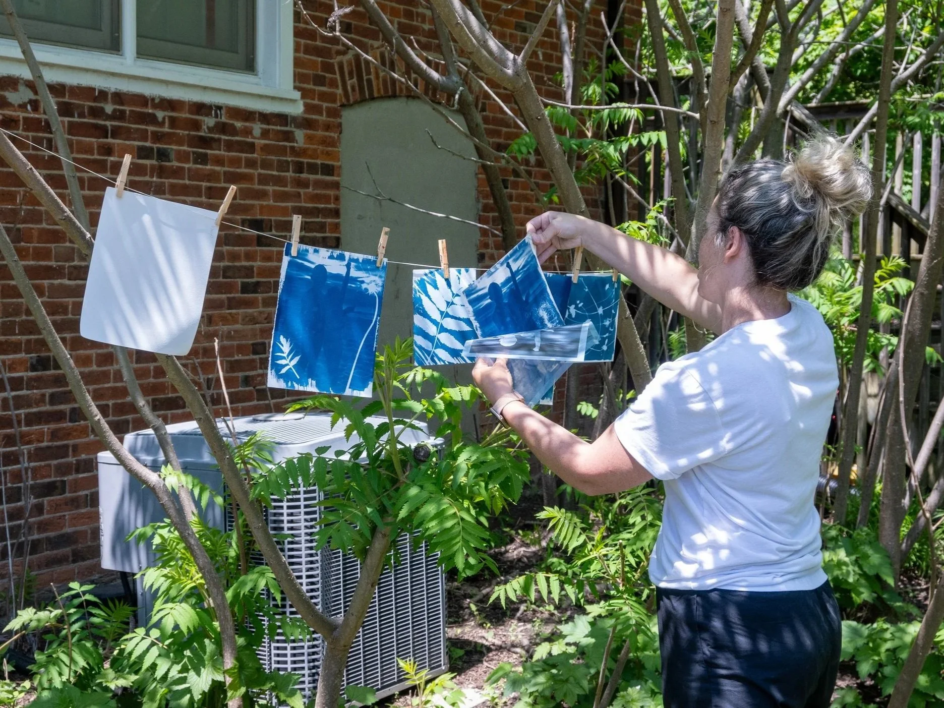 A person hangs blue cyanotype prints on a clothesline.