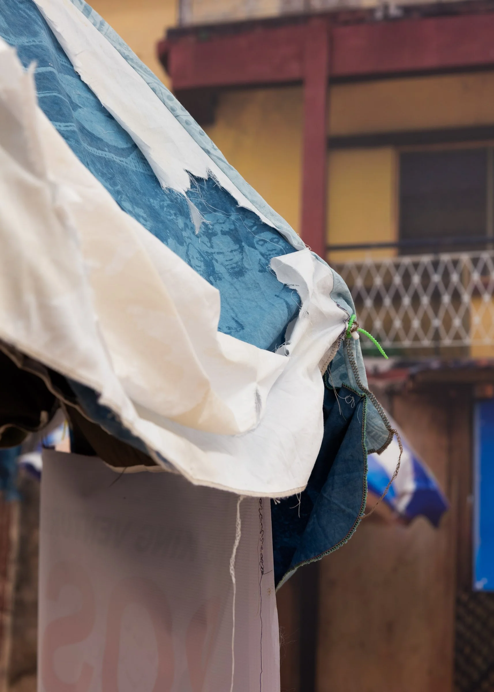 Close up of a street vendor umbrella with ripped fabric exposing a blue, hand-dyed archival photo of a group of Nigerian women. 