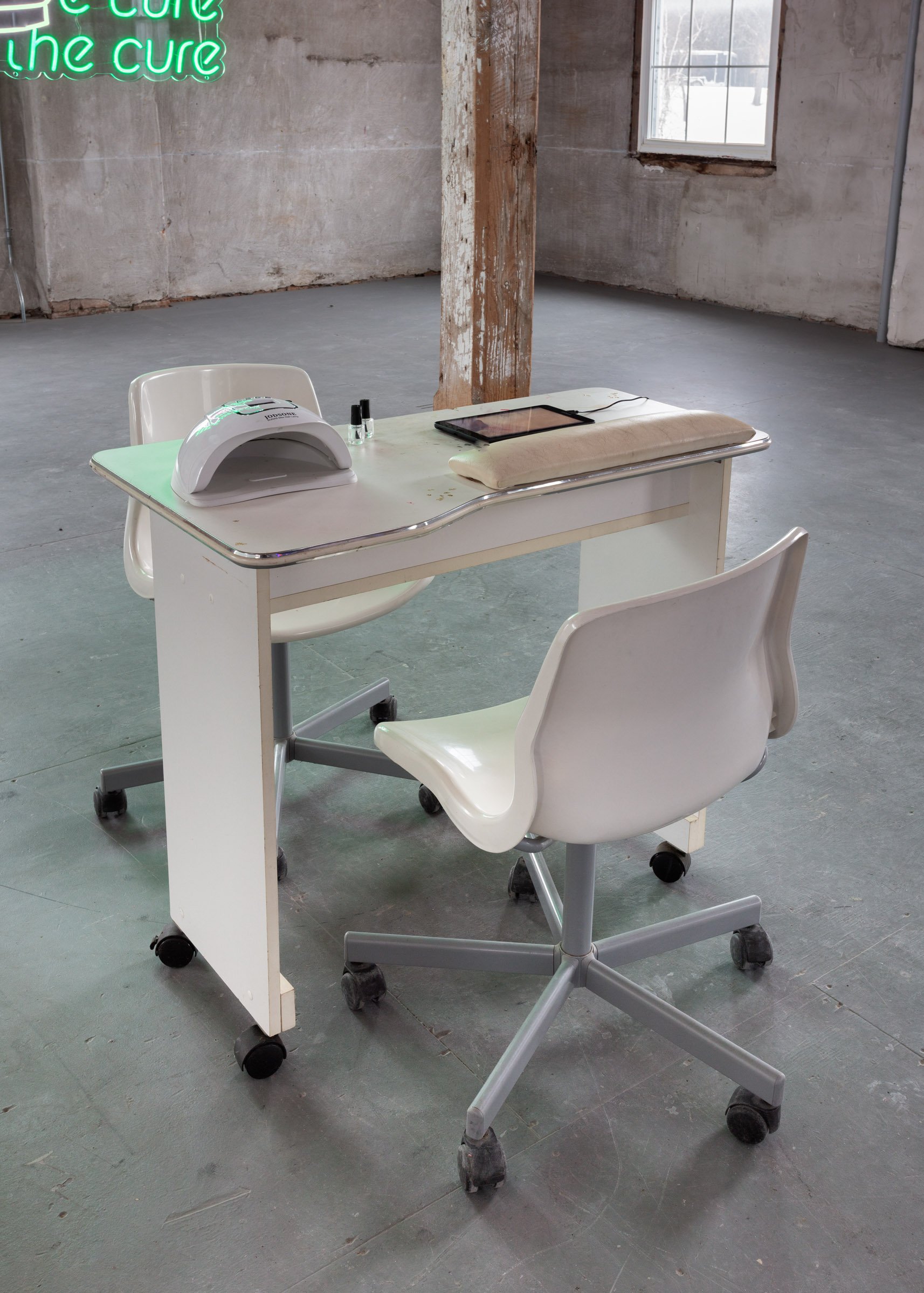 White table with nail polish and a LED gel curing lamp placed on top with a white chair on either side, resembling a nail salon.