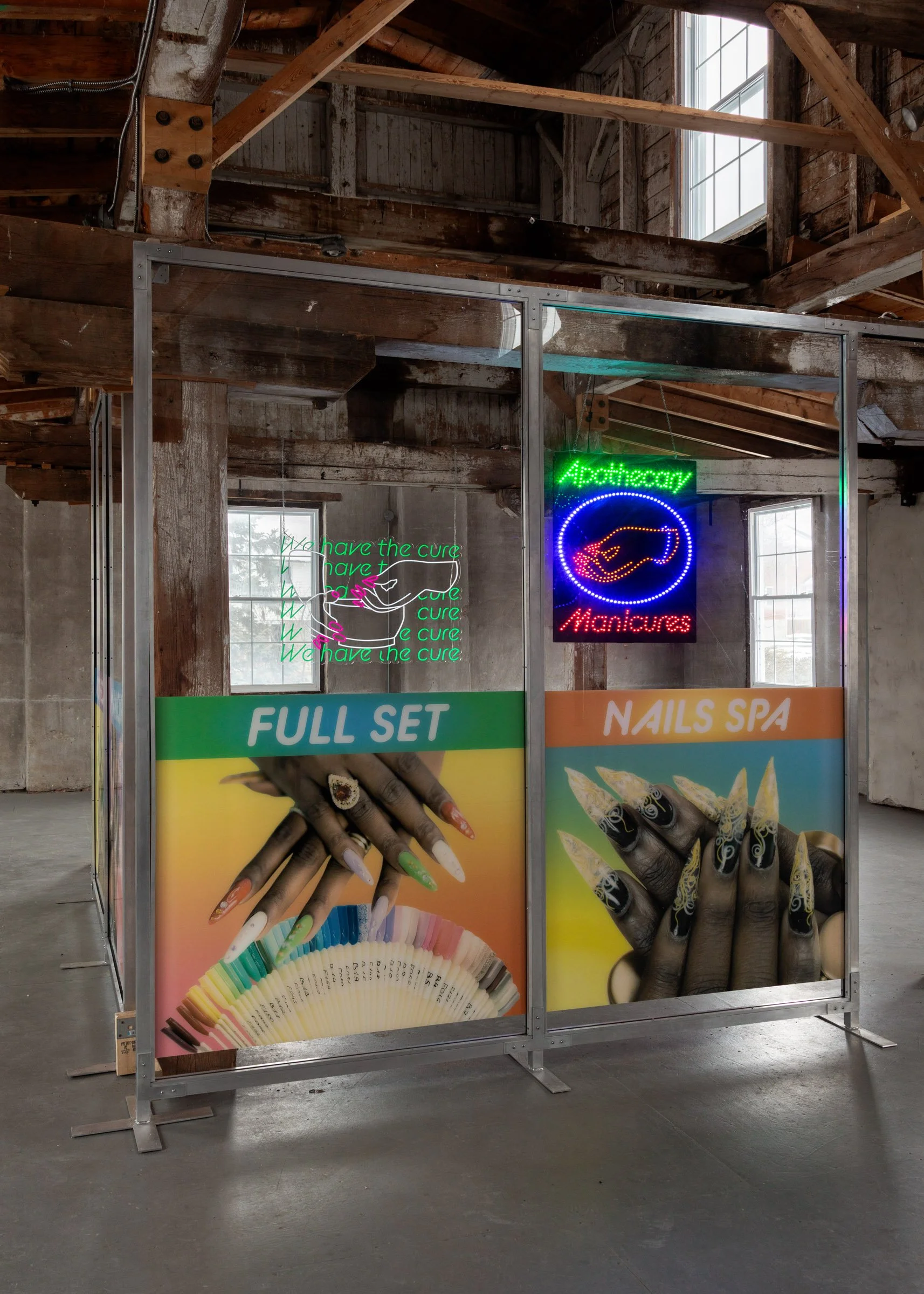 Installation that resembles the exterior windows of a nail salon with vibrant signs reading “Full Set” and “Nails Spa,” large photos of manicured hands with long acrylic nails, and illuminated neon signs reading “Apothecary Manicures” and “We have th