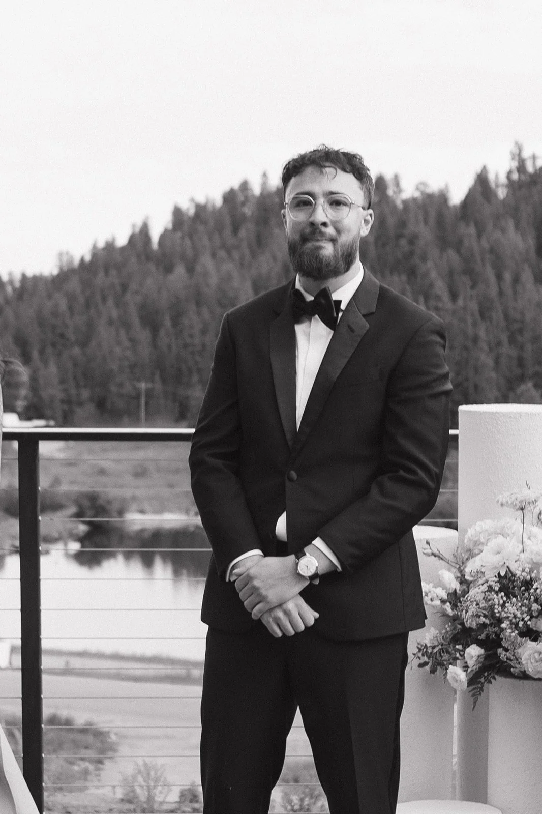 The groom stands in a tuxedo with mountains behind him, a calm moment just before the ceremony starts in his wedding day timeline.