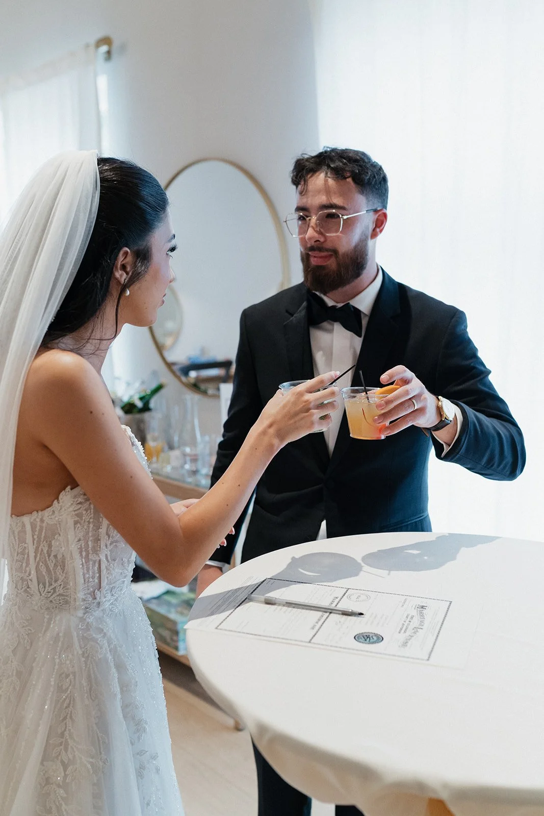 A bride and groom share a quiet toast over their marriage license, a sweet detail that’s perfectly timed in their wedding day timeline.
