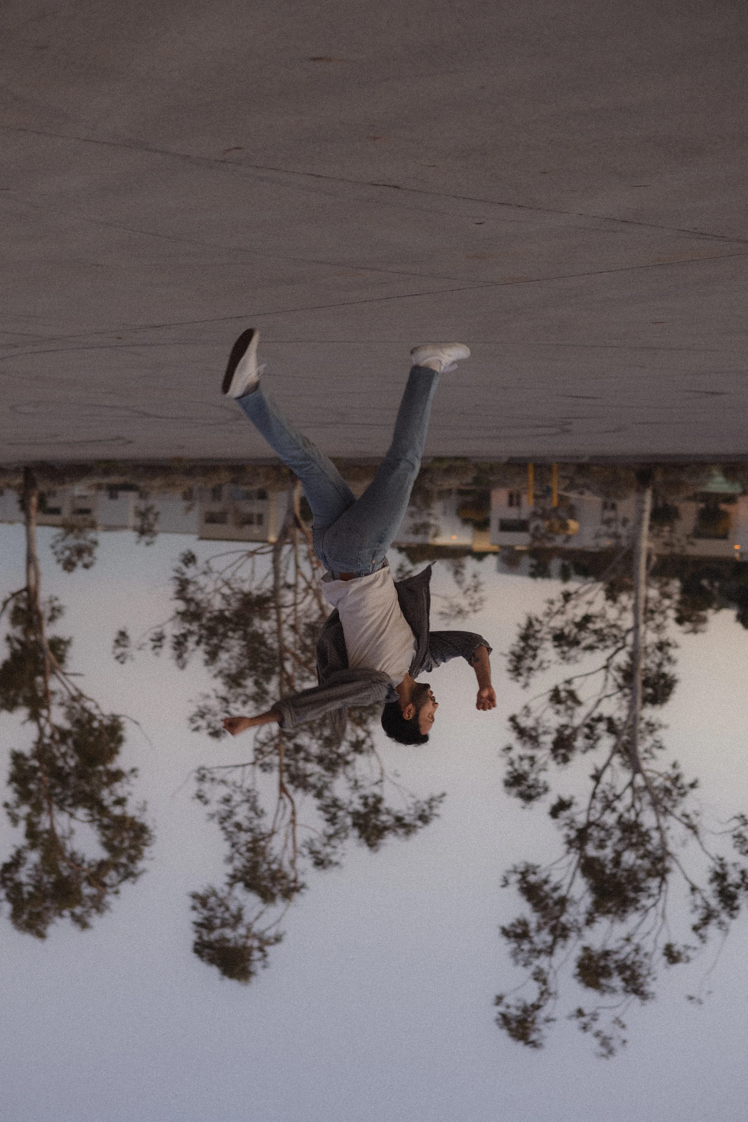 A person doing a handstand outdoors during dusk with trees and buildings in the background.