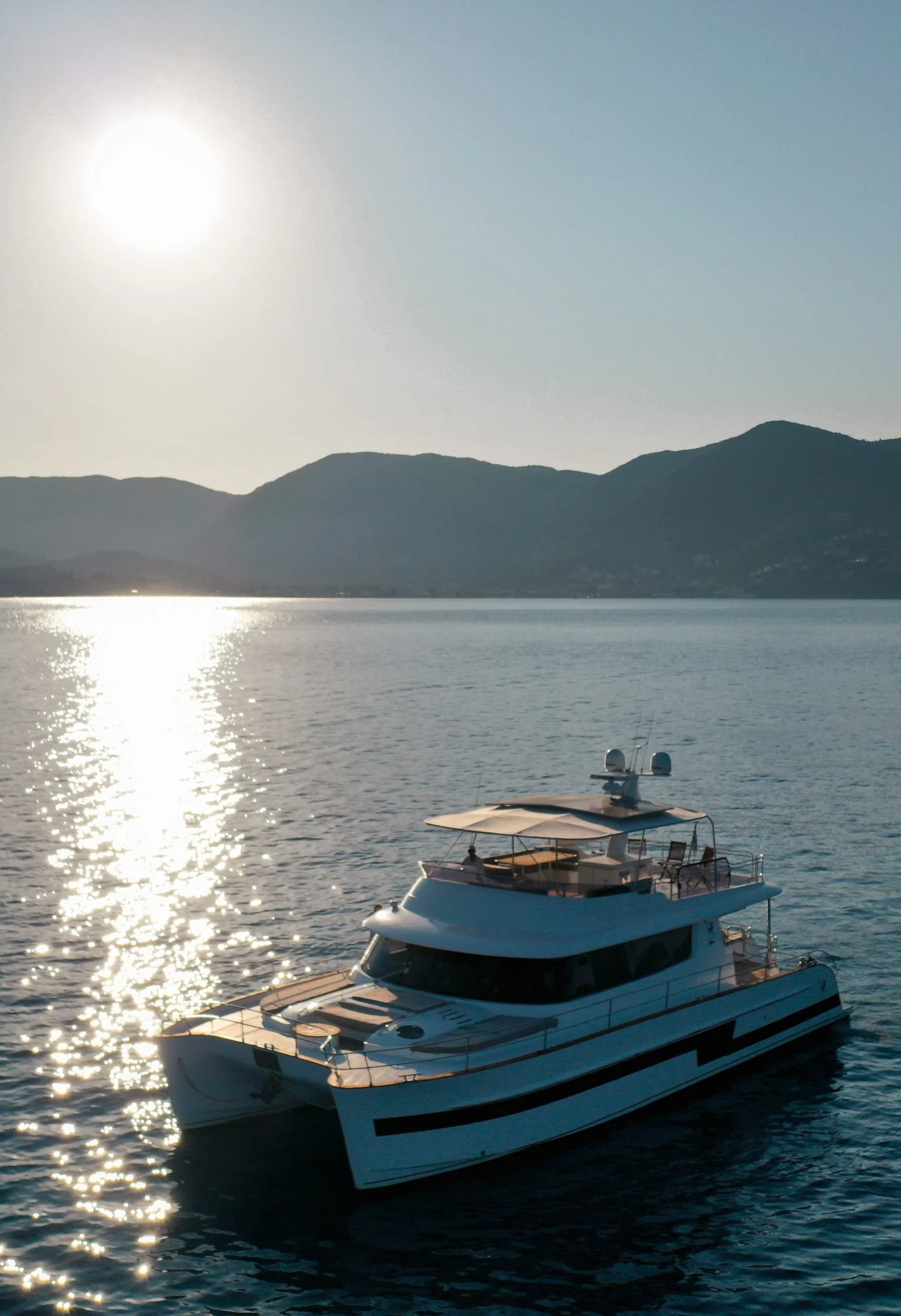 A yacht floating on a body of water during sunset or sunrise with mountains in the background.