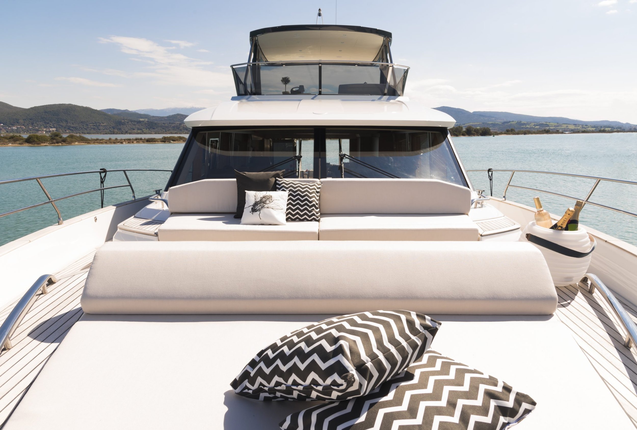 View of a luxurious yacht with a spacious sun deck, outdoor cushions, and a view of the water with mountains in the background.