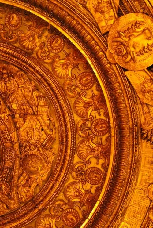 Ornate, gold-colored ceiling with detailed carvings and medallions, part of a historic or religious building.