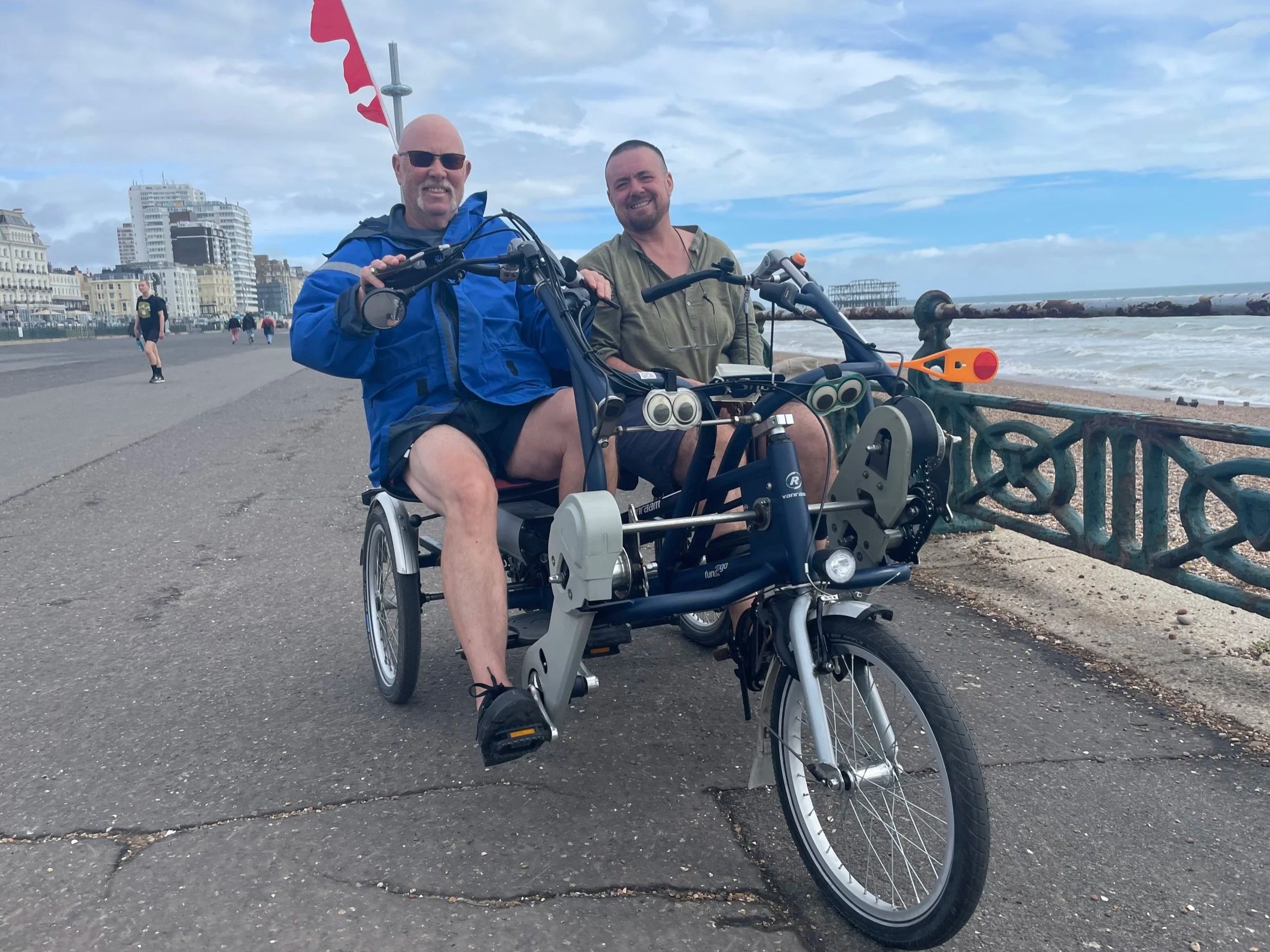 Two people cycling a side-by-side tandem, with the sea in the background.