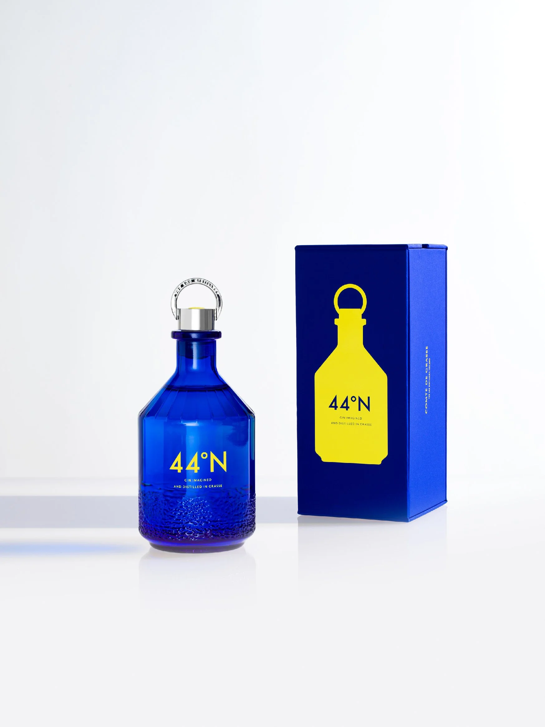 A blue glass bottle with yellow text and a silver cap next to a matching blue box with yellow graphic and text, both displaying the brand "44°N"