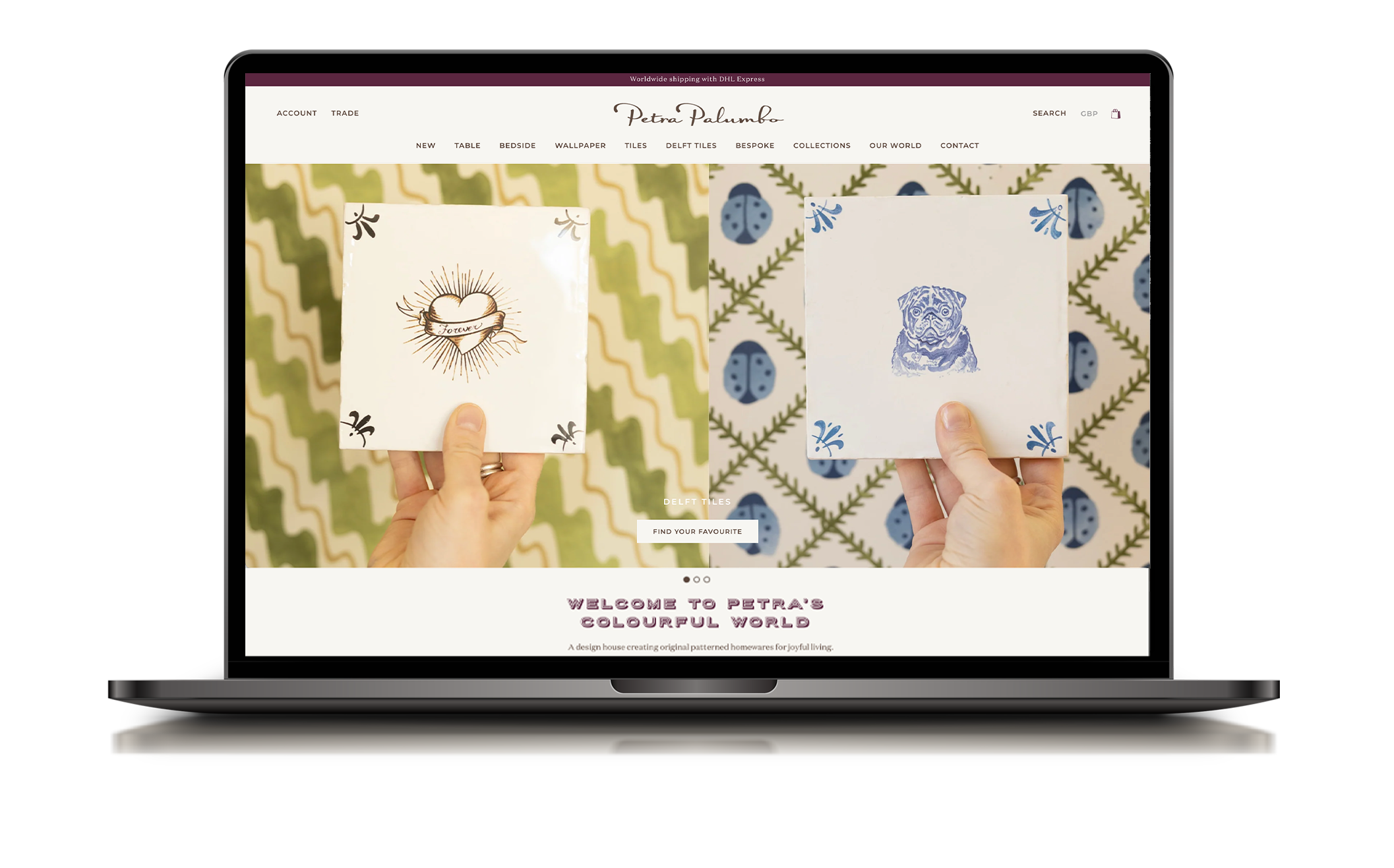 Laptop displaying website with two hand-held decorative tiles, one with a heart and the word "forever," and the other with a dog illustration, against patterned backgrounds.