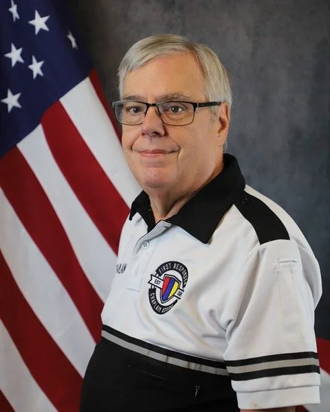 A woman in a police uniform standing in front of an American flag.