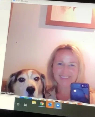 A woman with blonde hair smiling and taking a selfie with her dog during a video call on a computer screen.