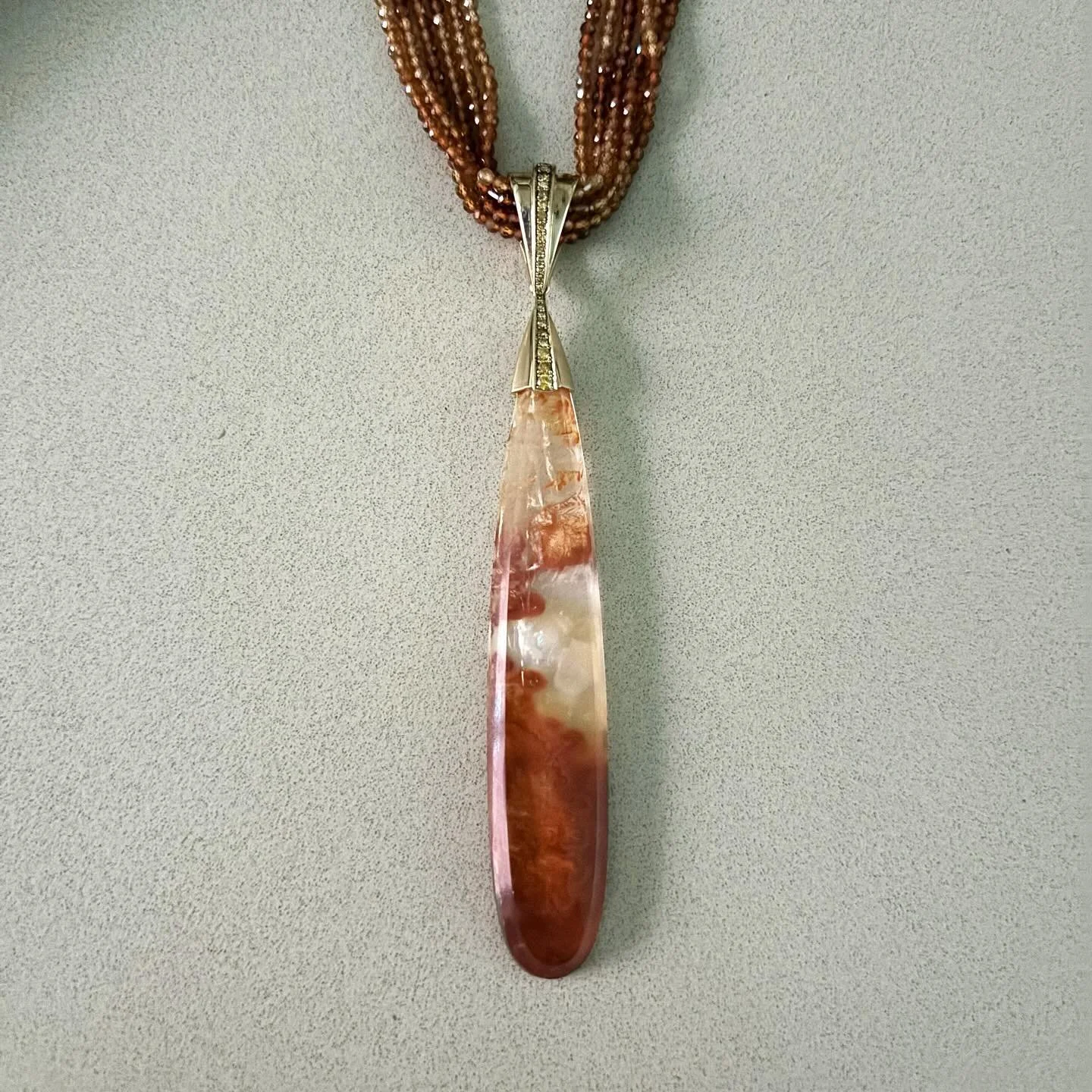 An elegant Carnelian pendant suspended from a necklace of finely faceted matching Carnelian beads. The warm tones of the stone are complemented by the richness of 18K gold, further enhanced by the subtle brilliance of yellow diamonds. A piece that se