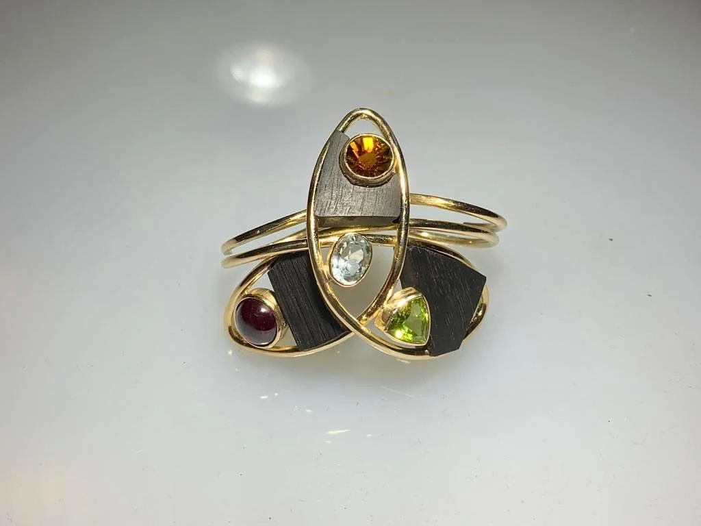 A whimsical two finger ring adorned with pieces of ebony, tourmalines, and held together by an 18kt yellow gold structure.