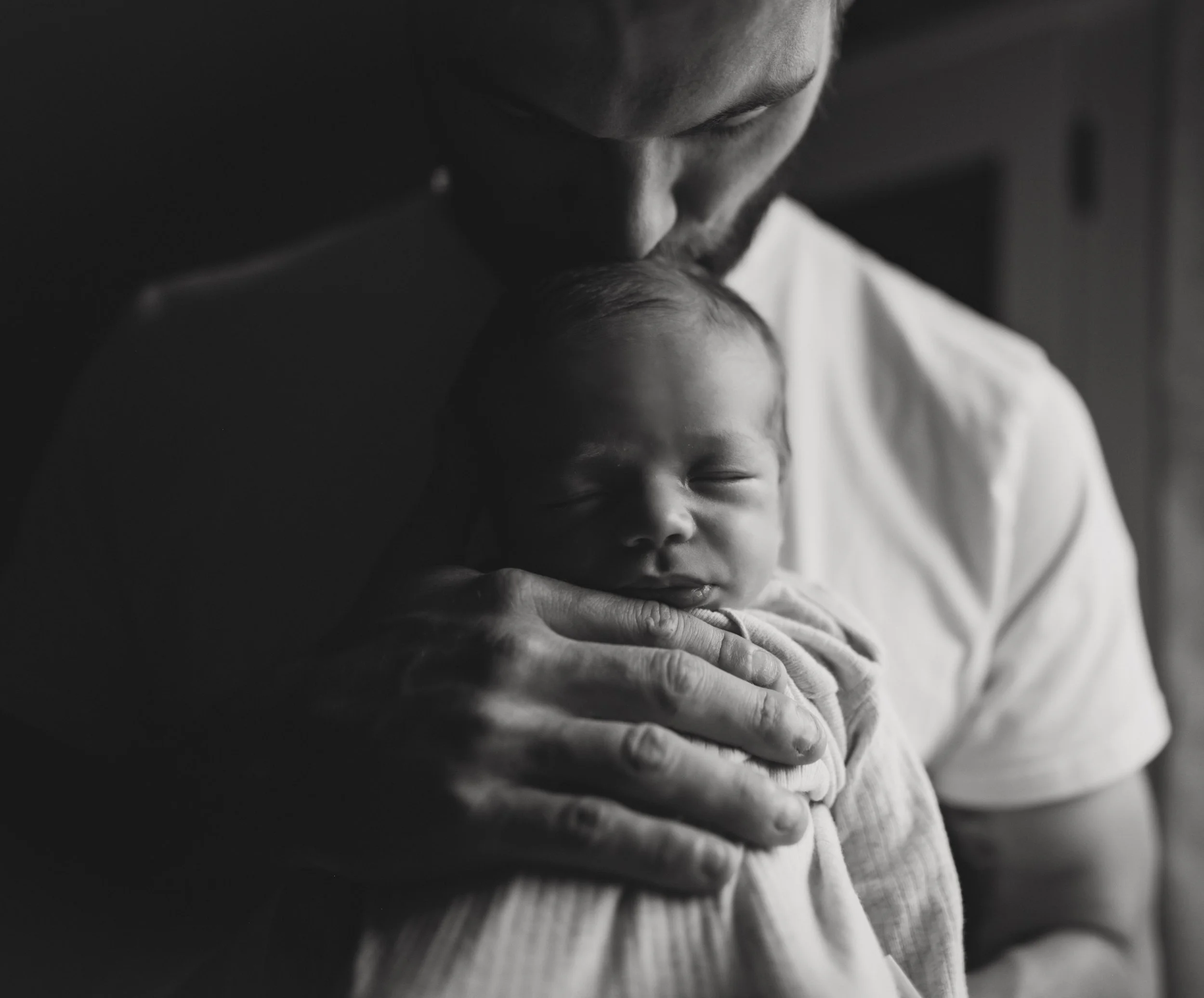 Black and white photo of a man holding a sleeping baby close to his chest, with the baby's face nestled into the man's shoulder.