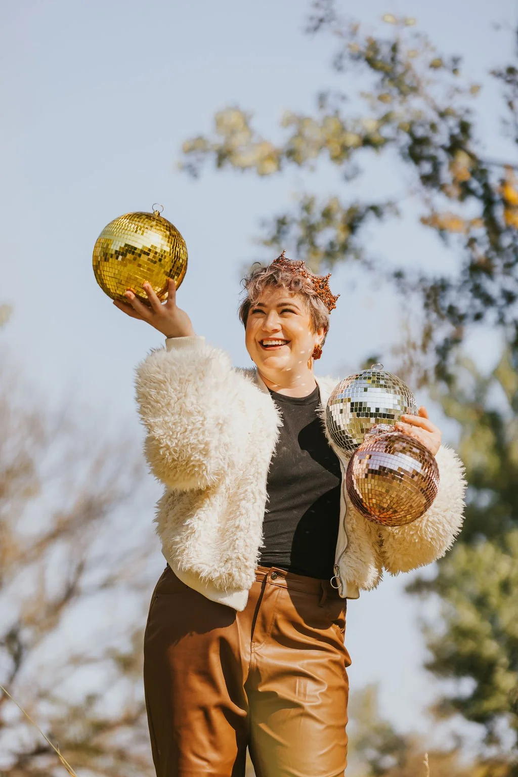 Person in a fluffy white jacket holding shiny disco balls outdoors.