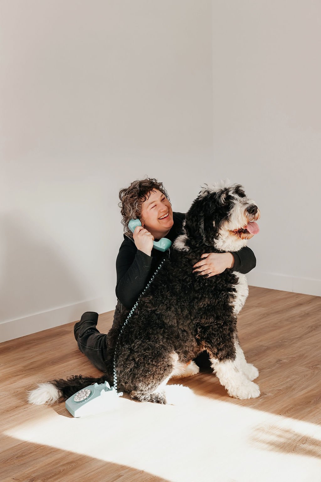 Person lying on the floor smiling at a fluffy white dog in a living room with a yellow chair and blue sofa in the background.