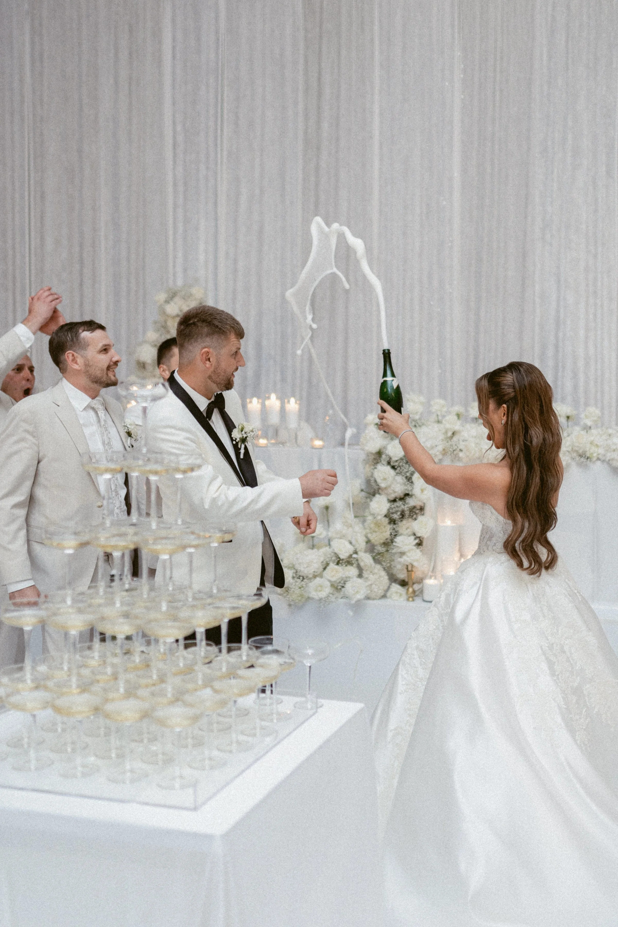 Bride pouring champagne into a coupe tower during the wedding reception.